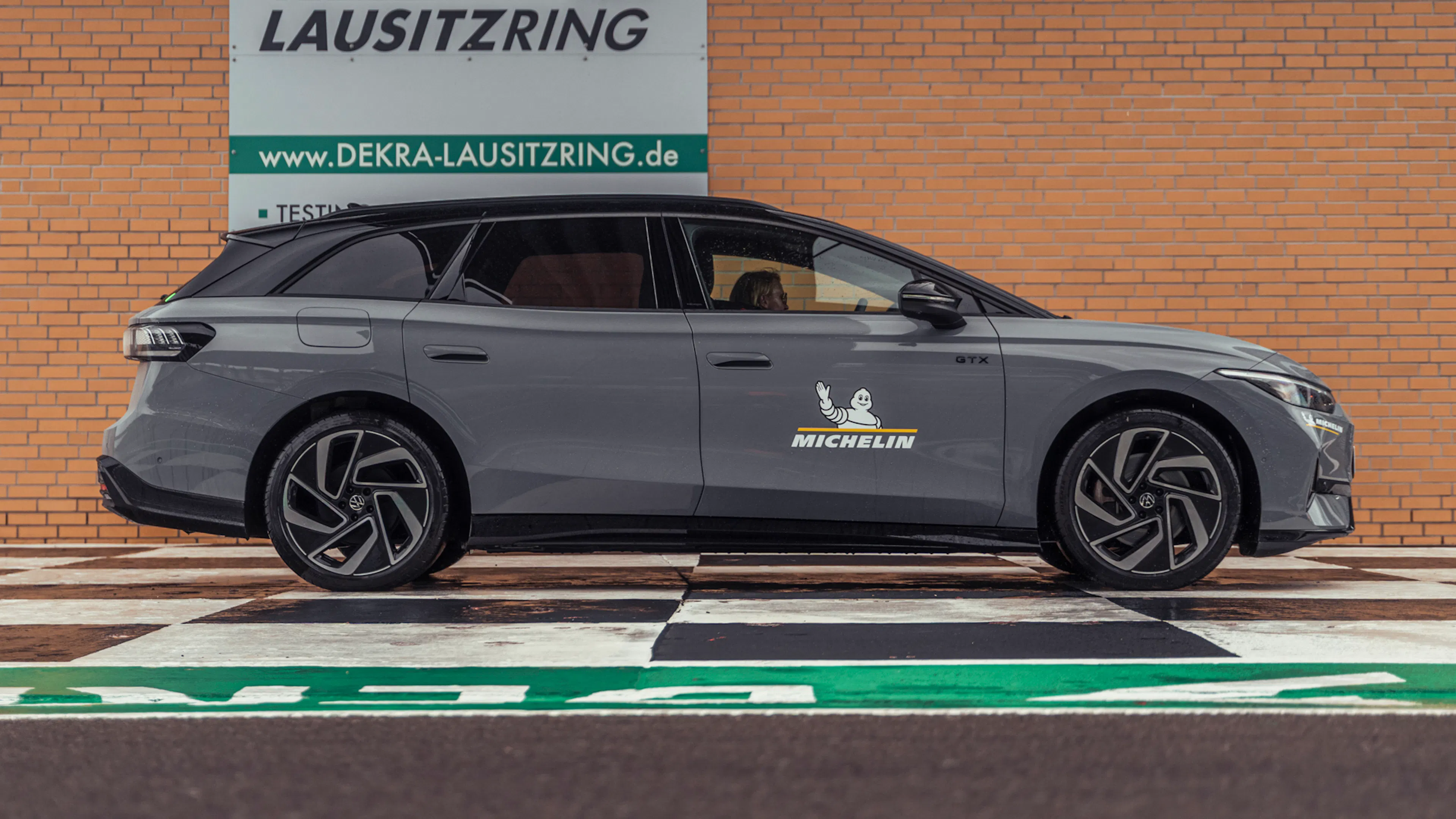 Heckansicht eines grauen VW ID.7 Tourer GTX auf einer nassen Rennstrecke.