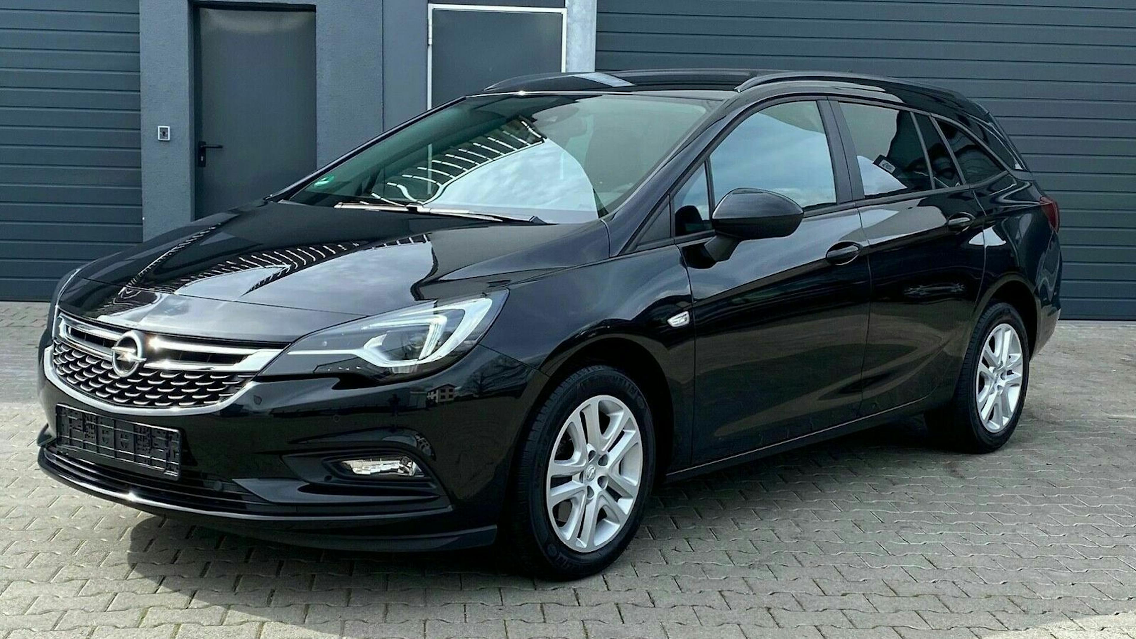 Schwarzer Kombi-Pkw, steht auf einem gepflasterten Hof vor einem grauen Garagentor. Die Fenster sind dunkel getönt, und der Himmel ist bewölkt.