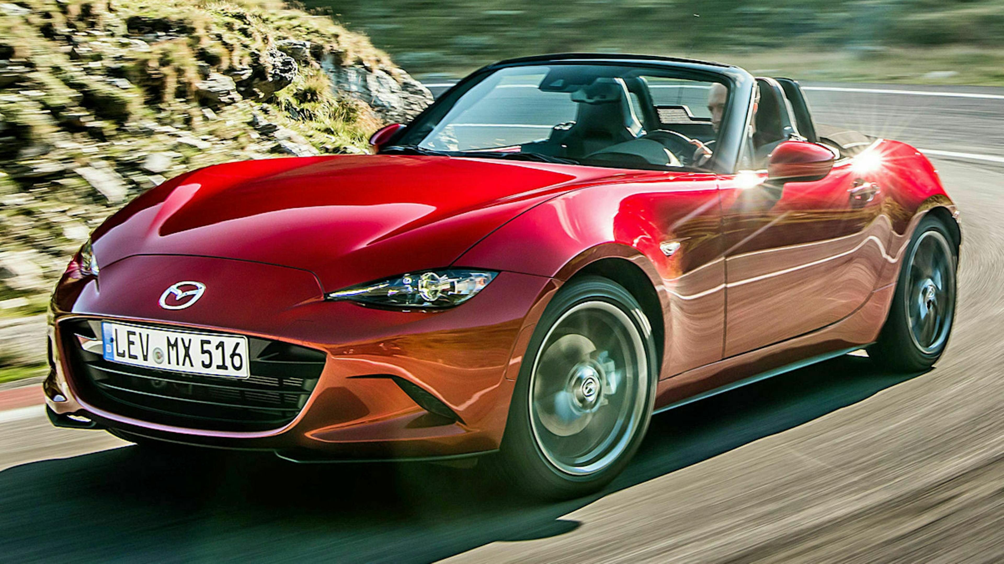 Ein roter Mazda MX-5 mit Heckantrieb fährt eine kurvige Bergstraße entlang