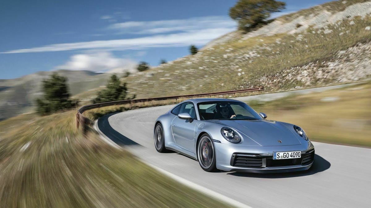 Ein silberner Porsche 911 fährt eine kurvige Bergstraße entlang