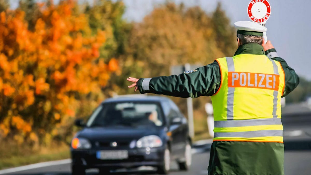 Ein Polizist winkt in Warnweste gekleidet einen Autofahrer von der Straße in eine Haltebucht.