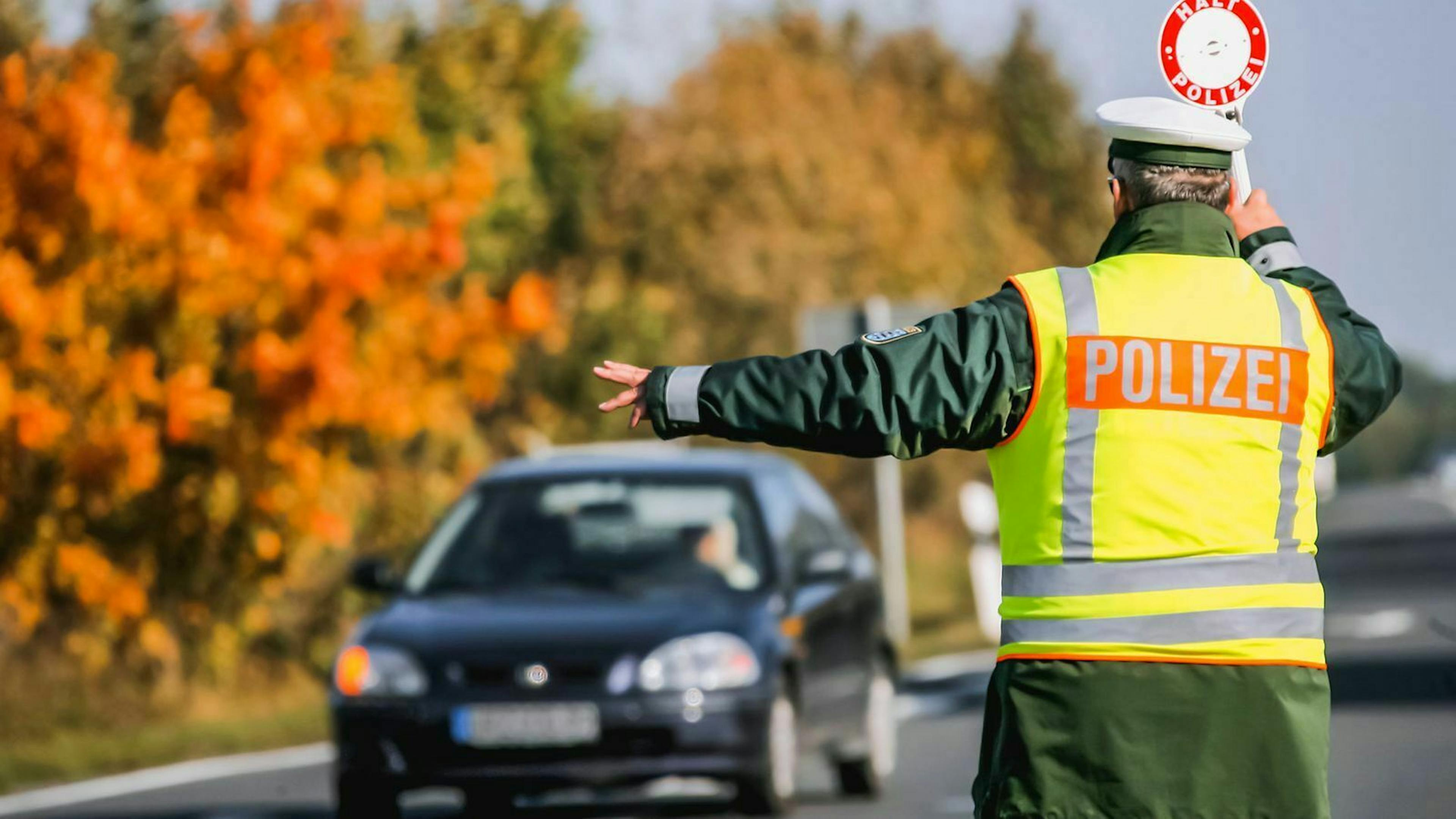 Ein Polizist winkt in Warnweste gekleidet einen Autofahrer von der Straße in eine Haltebucht.