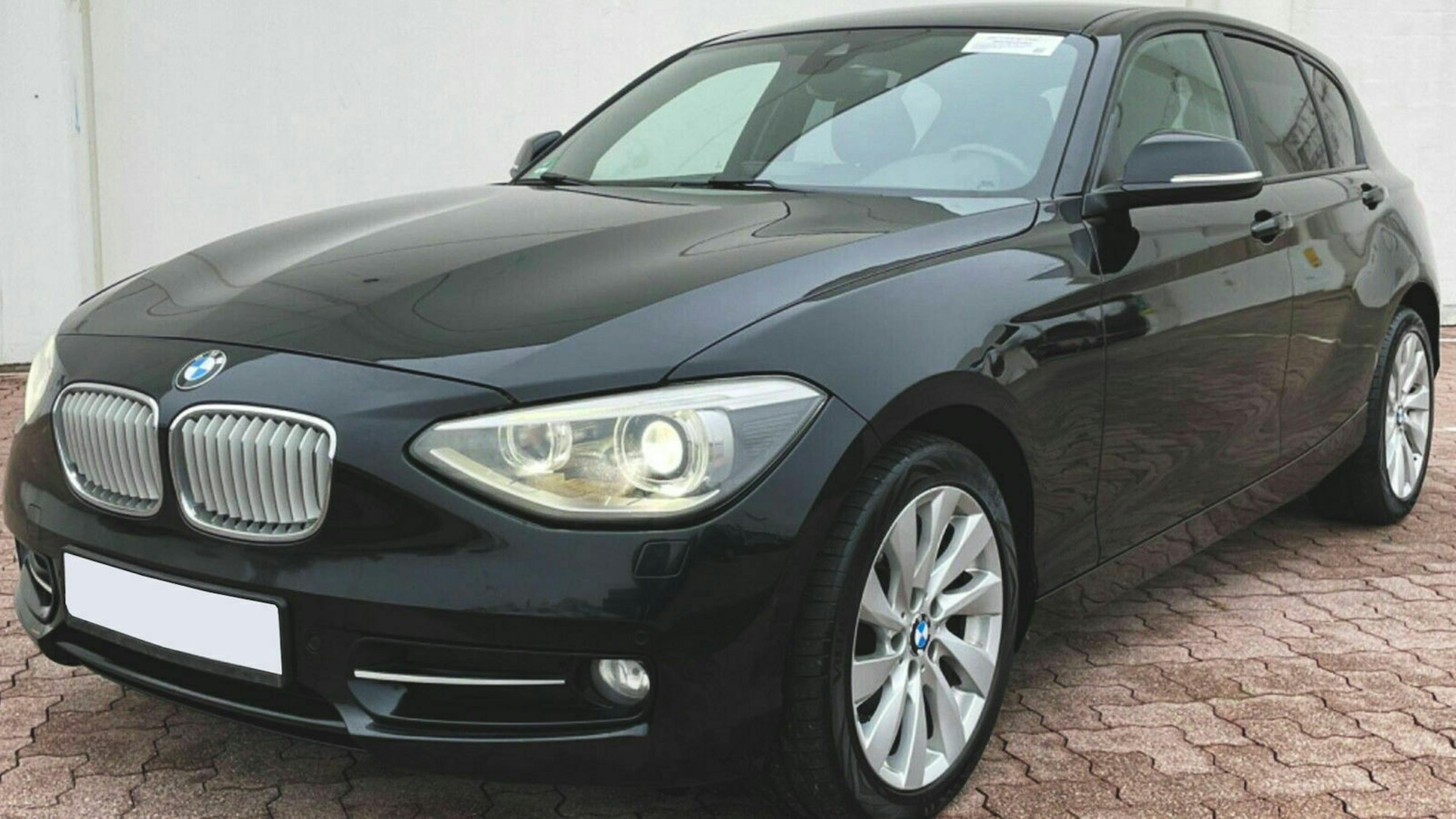 Ein schwarzer BMW 1er mit Heckantrieb steht vor einer weißen Wand