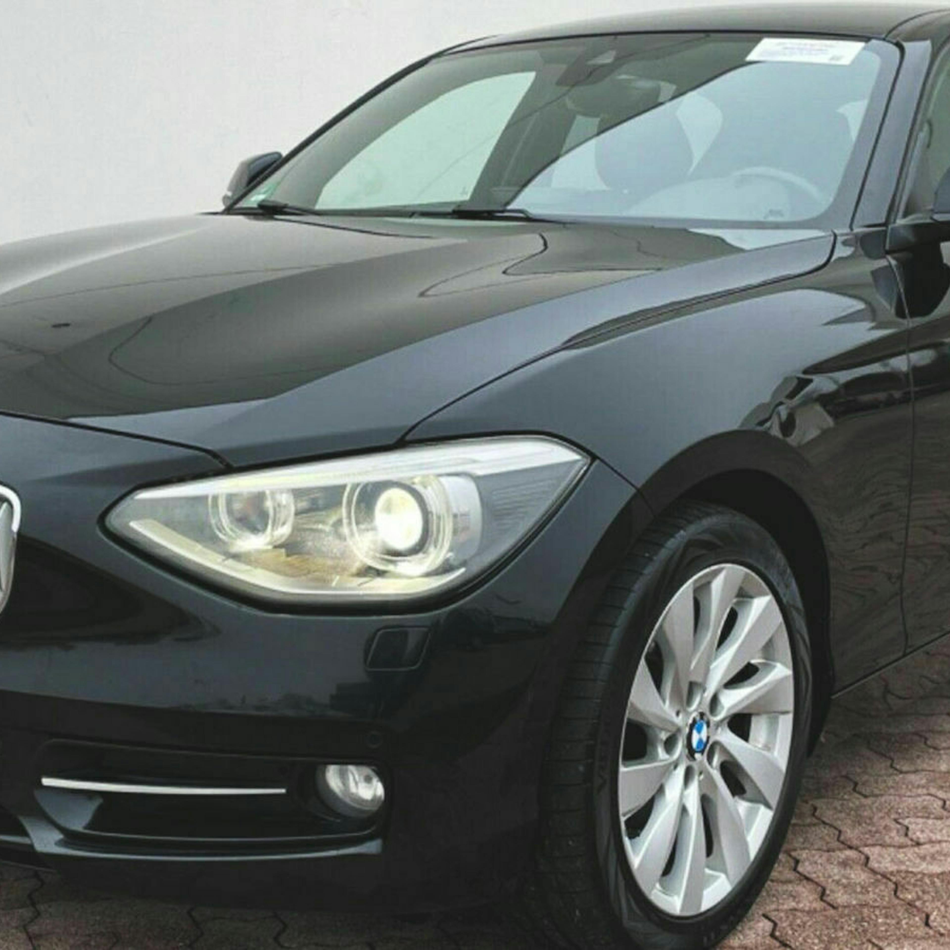 Ein schwarzer BMW 1er mit Heckantrieb steht vor einer weißen Wand