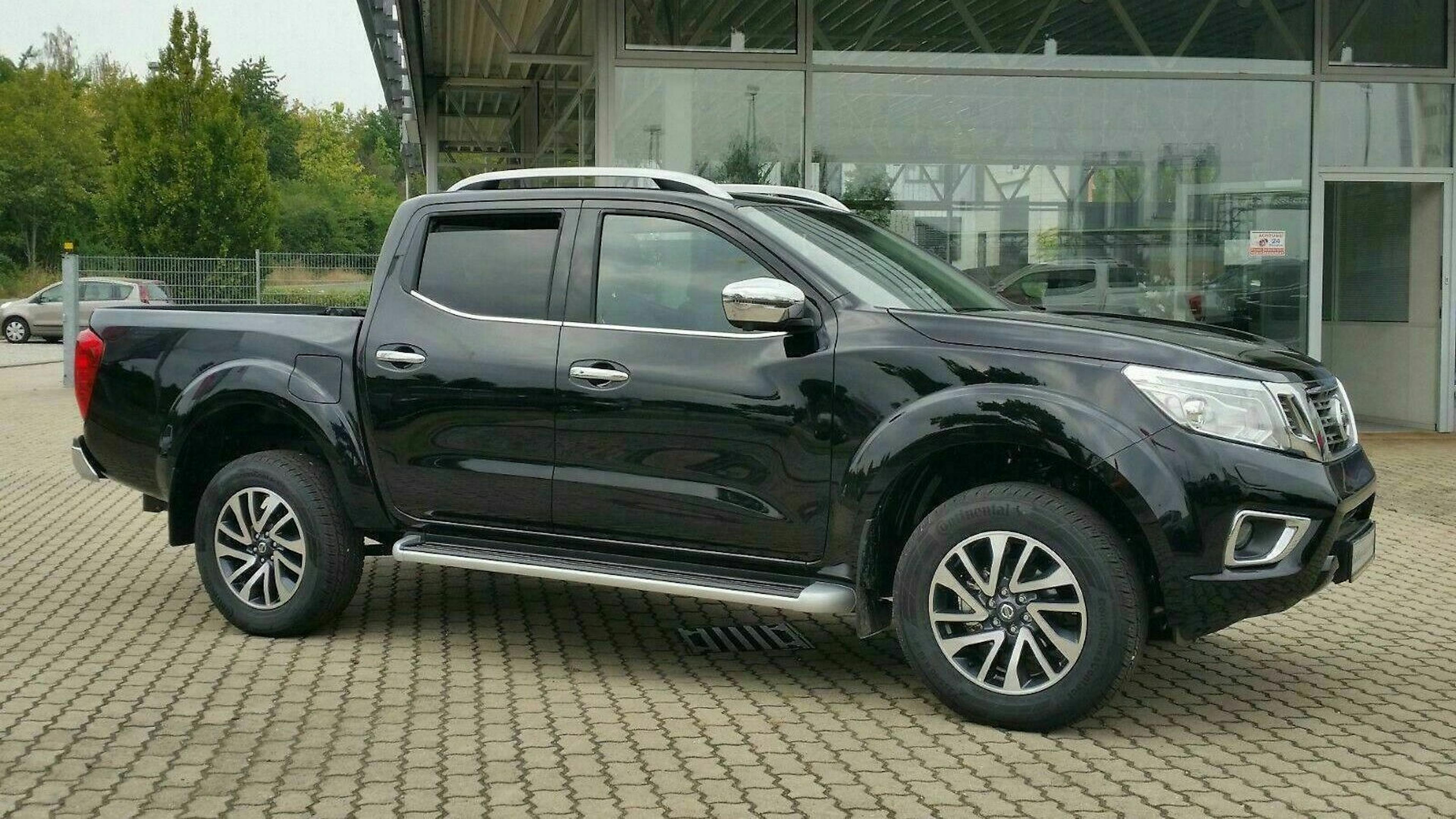 Ein schwarzer Nissan Navara Pick-up steht vor einem Gebäude mit Glasfront.