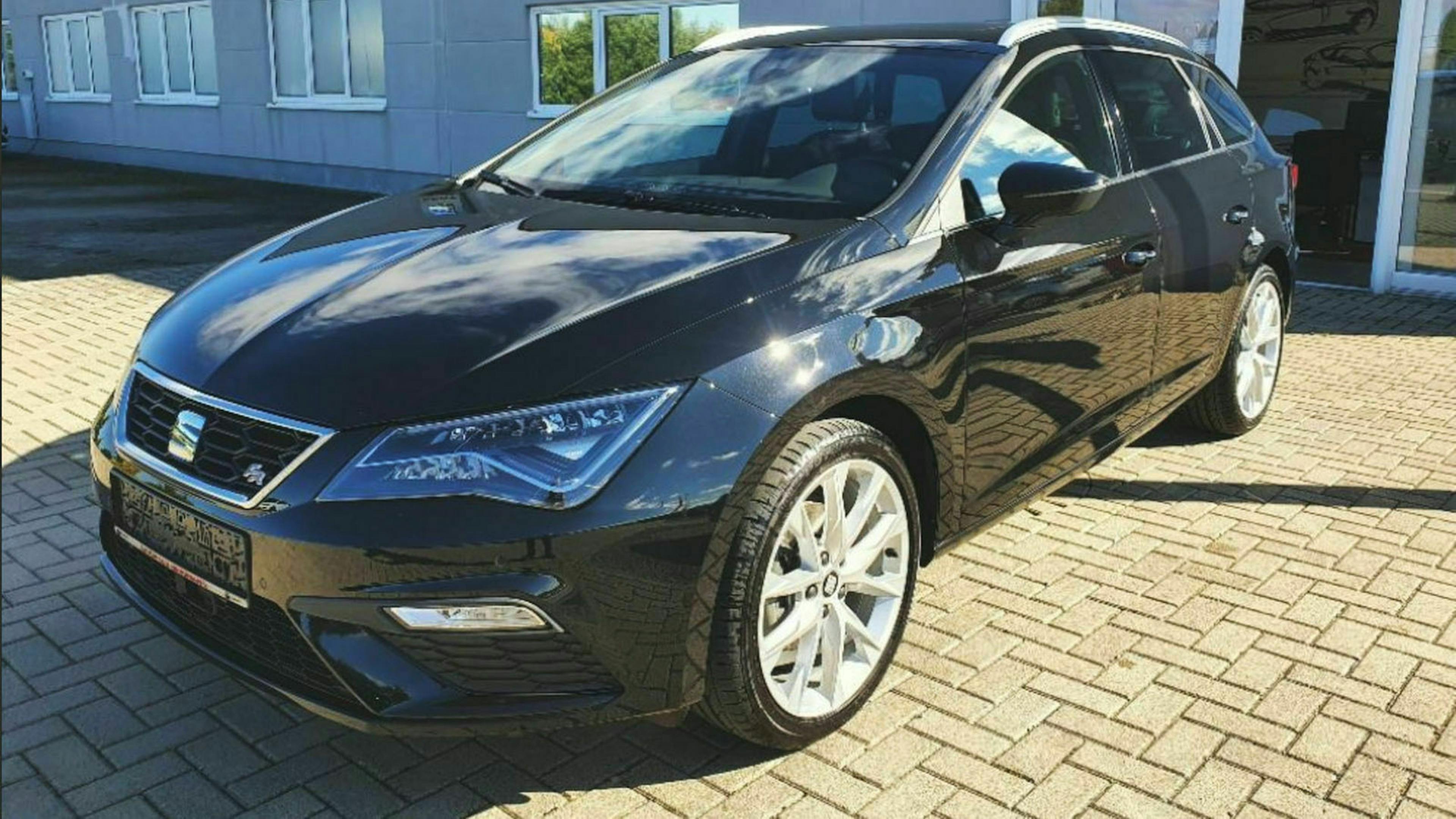 Ein schwarzer Seat Leon steht auf einem Parkplatz vor einem Gebäude mit hellgrauer Fassade