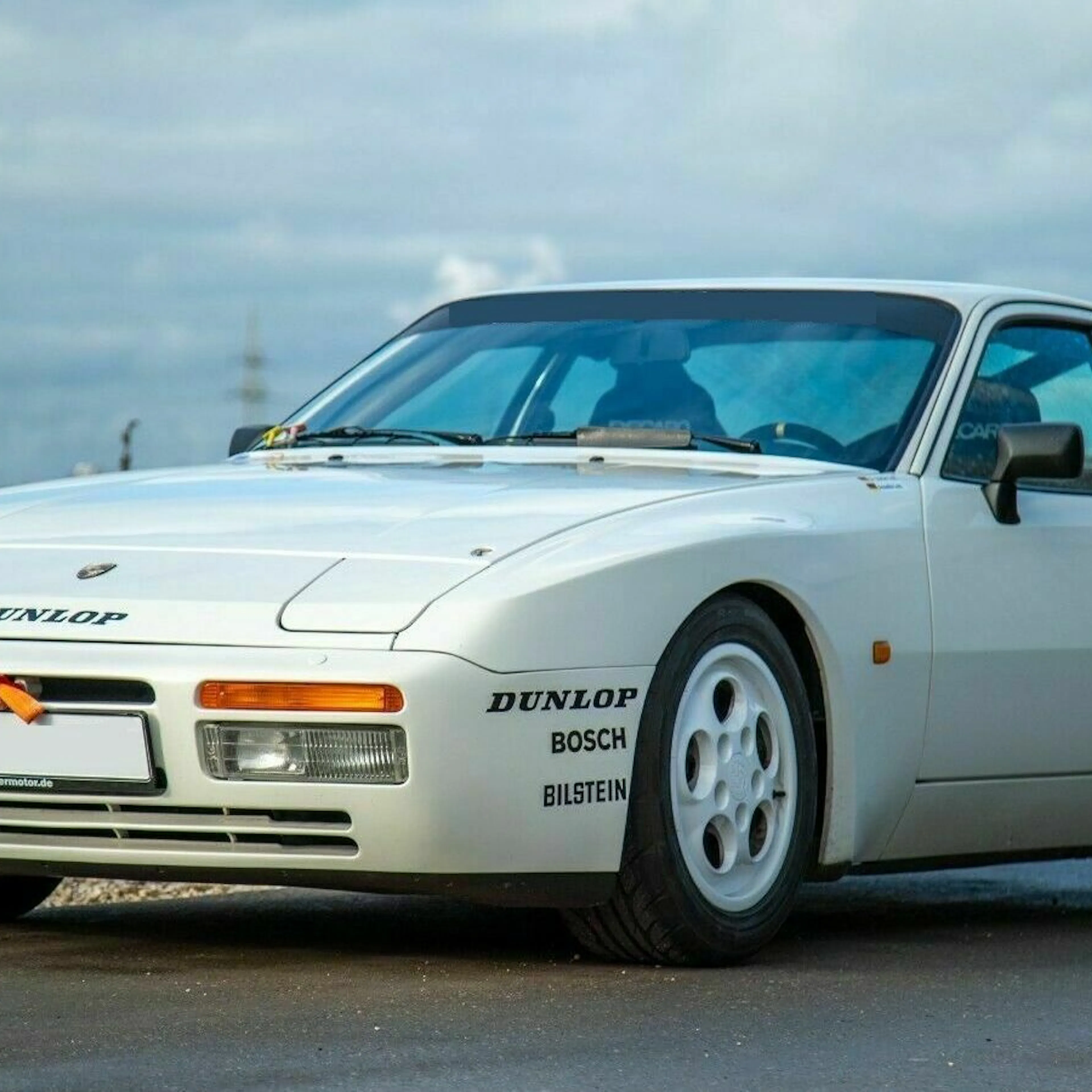 Ein weißer Porsche 944 Oldtimer steht am Straßenrand einer Landstraße.