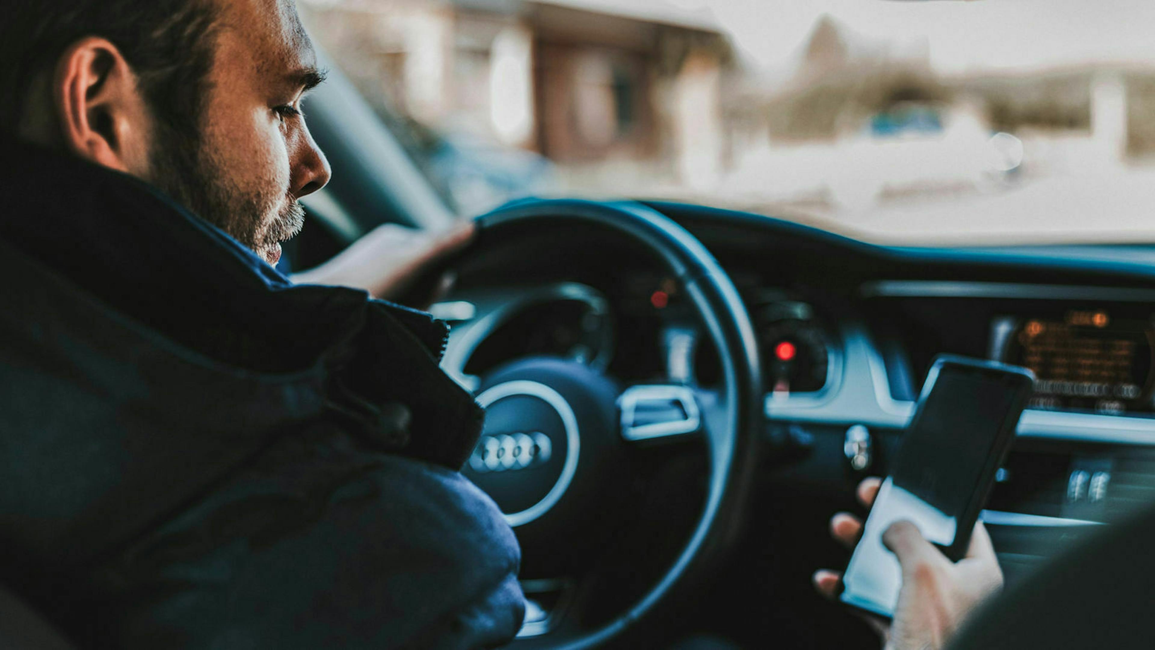 Jemand sitzt am Lenkrad eines Autos und schaut auf sein Mobiltelefon