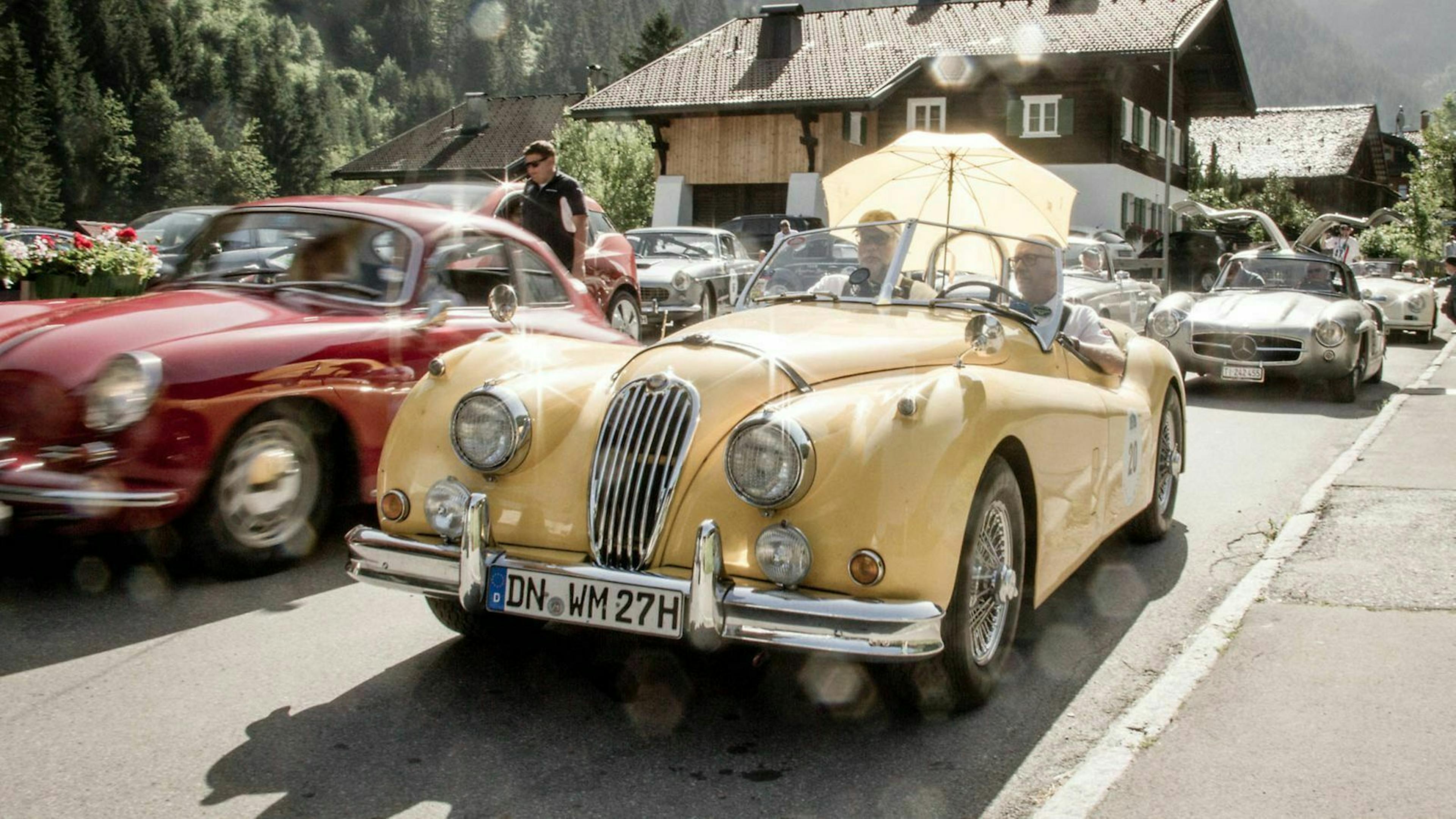 Ein beige-gelber Roadster fährt an einem roten Sportwagen vorbei - beide Autos haben ein H-Kennzeichen.
