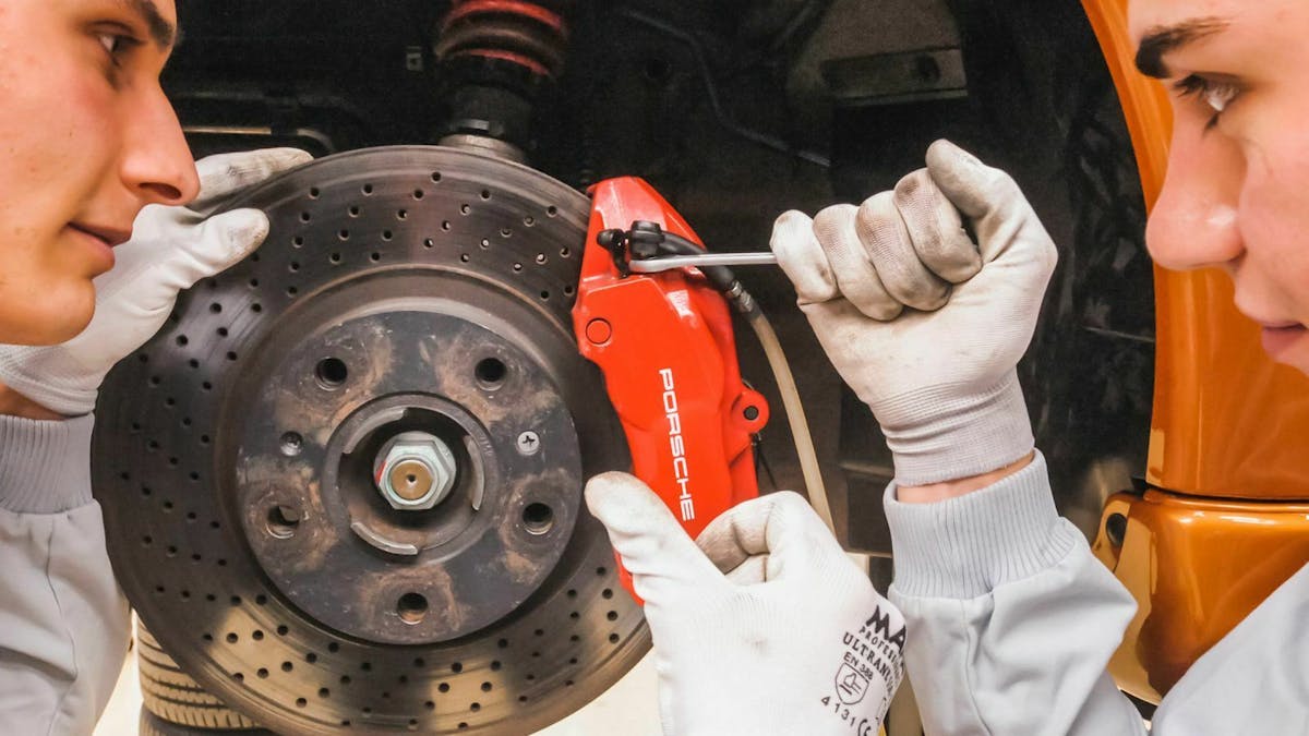Zwei Mechaniker inspizieren die Bremsanlage eines Porsche.