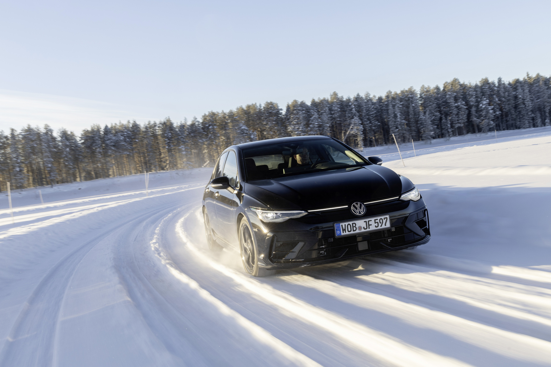 Schwarzer VW Golf mit Lichtband an der Front fährt über eine verschneite Straße vor Nadelwald.