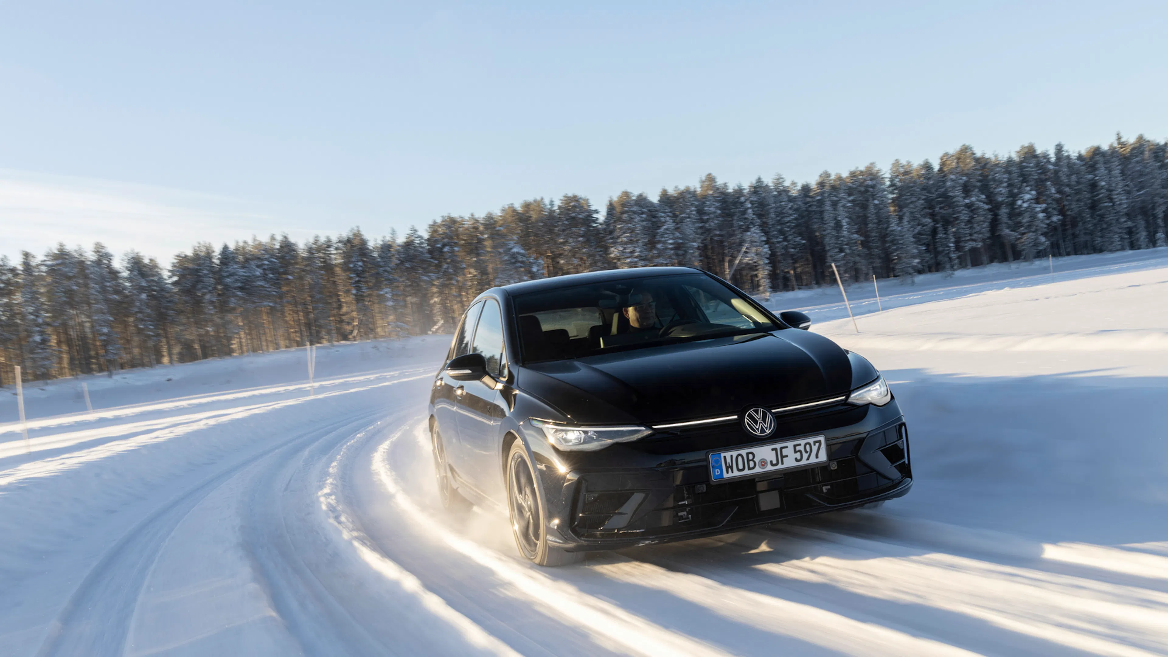 Schwarzer VW Golf mit Lichtband an der Front fährt über eine verschneite Straße vor Nadelwald.