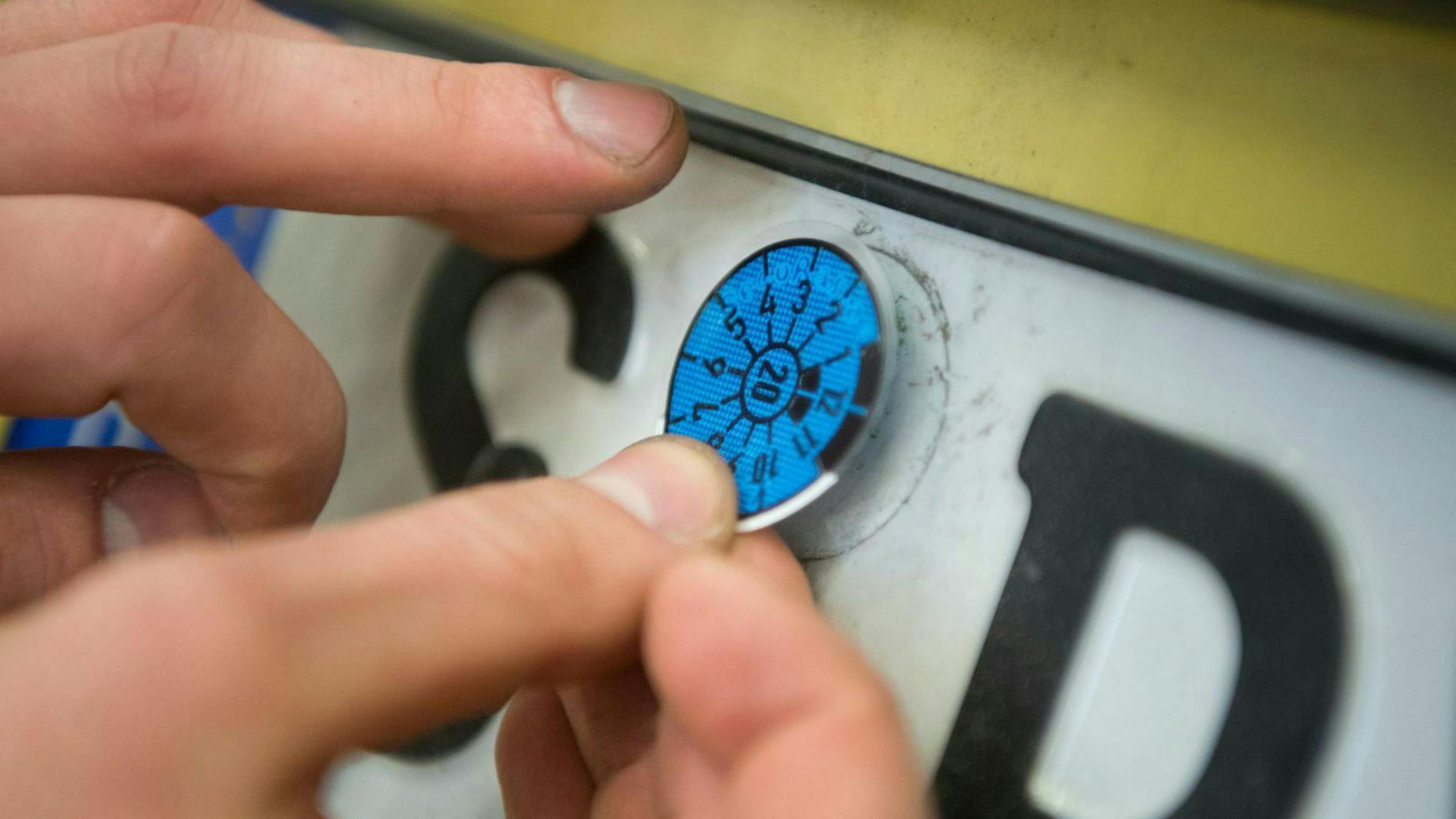 Eine Person klebt eine Plakette auf das Nummernschild eines Autos.