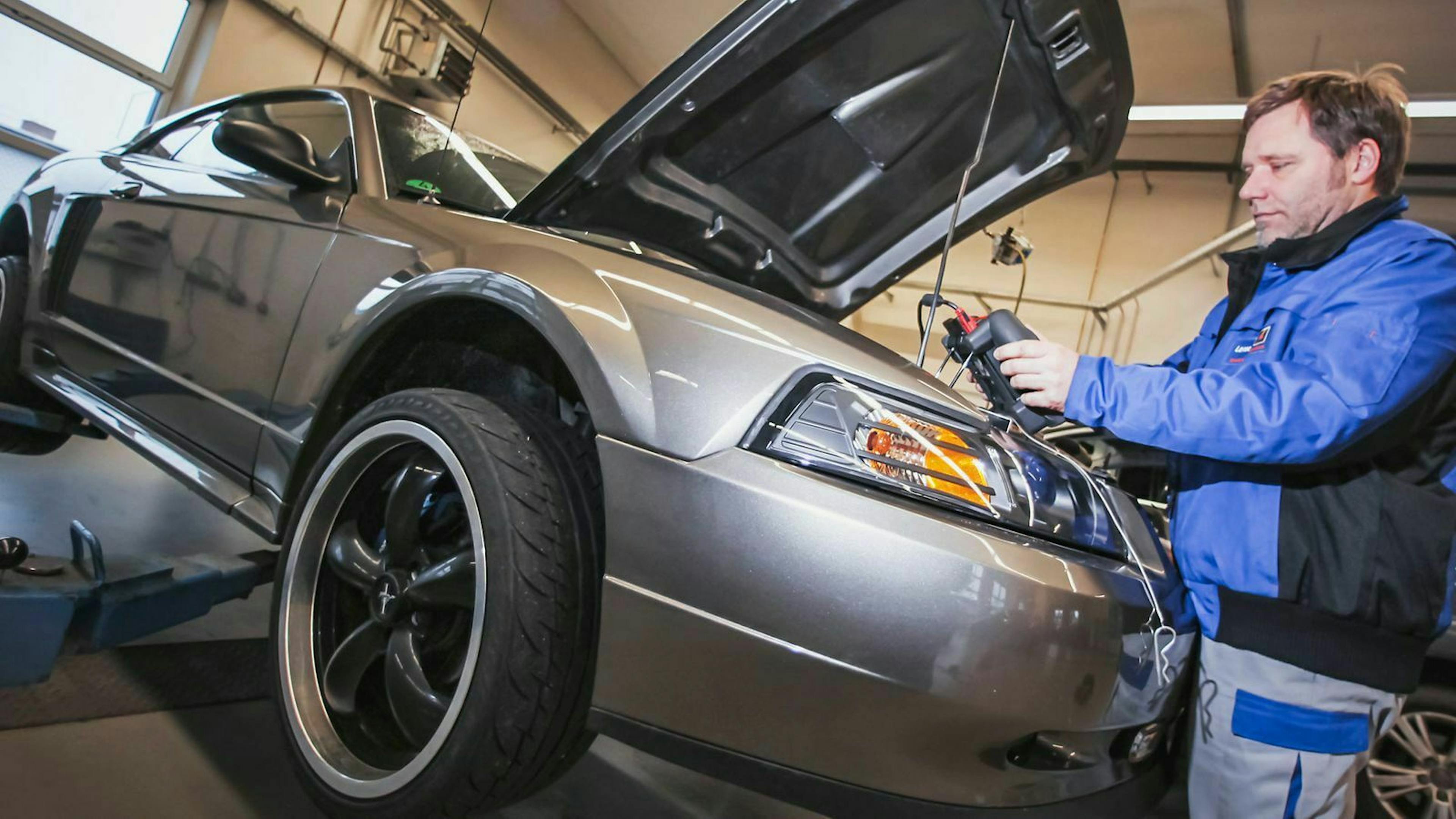 Ein Mechaniker steht an einem Ford Mustang, dessen Motorhaube geöffnet ist.