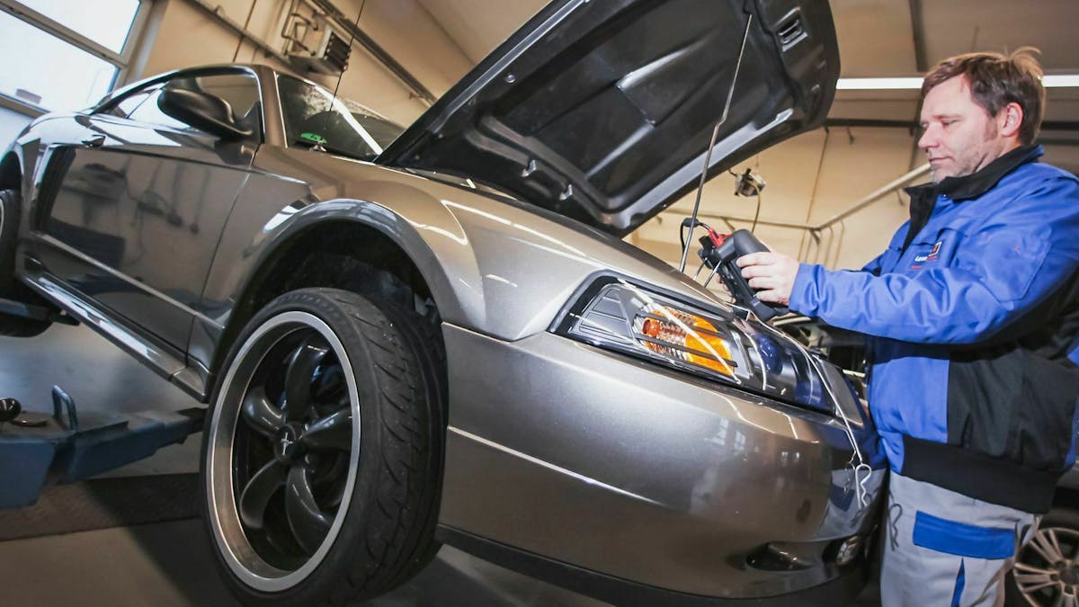 Ein Mechaniker steht an einem Ford Mustang, dessen Motorhaube geöffnet ist.
