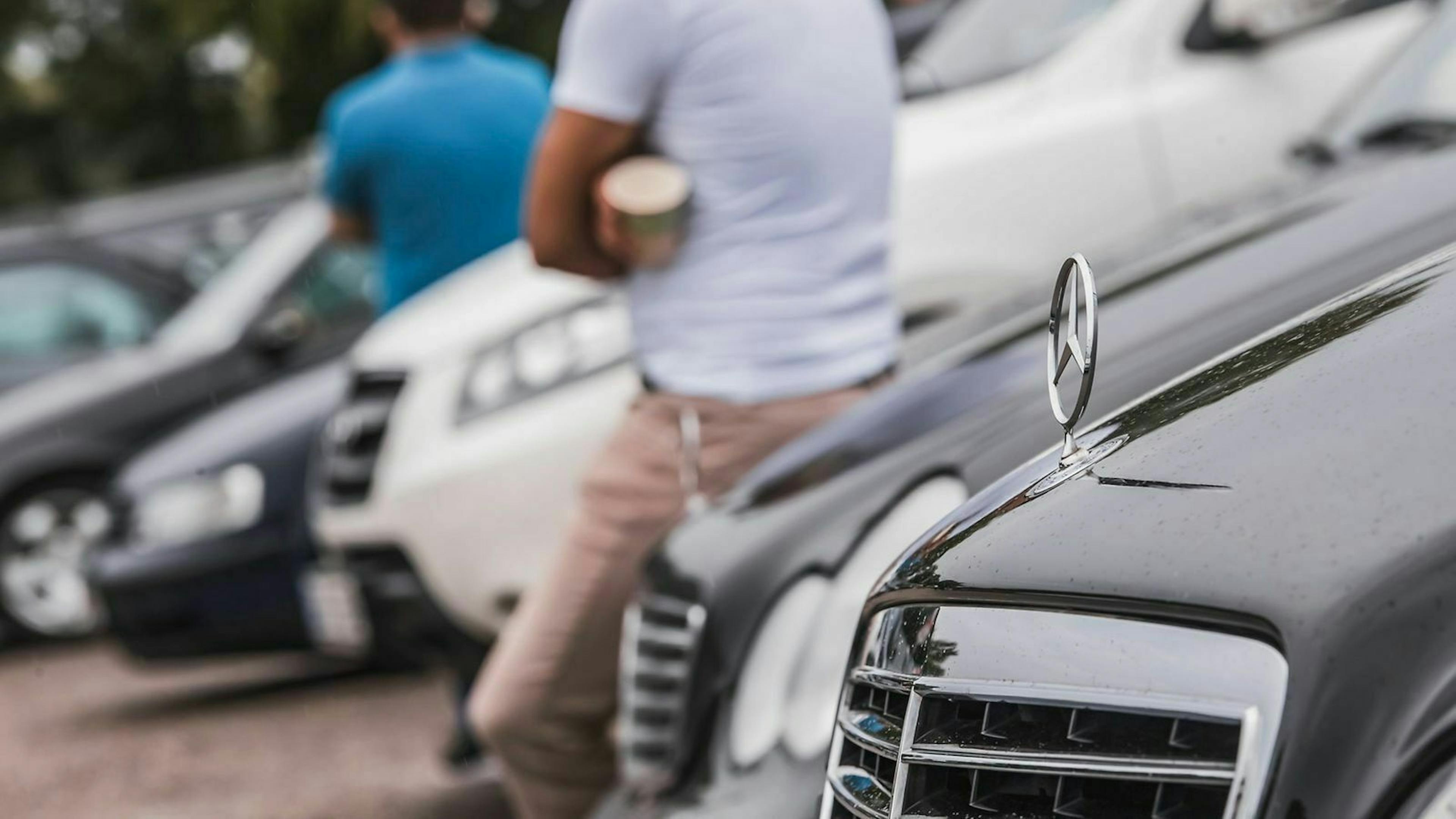 Zwei Verkäufer lehnen an Ihren Autos, die auf dem Hof einer mobile.de-Ankaufsstation parken.