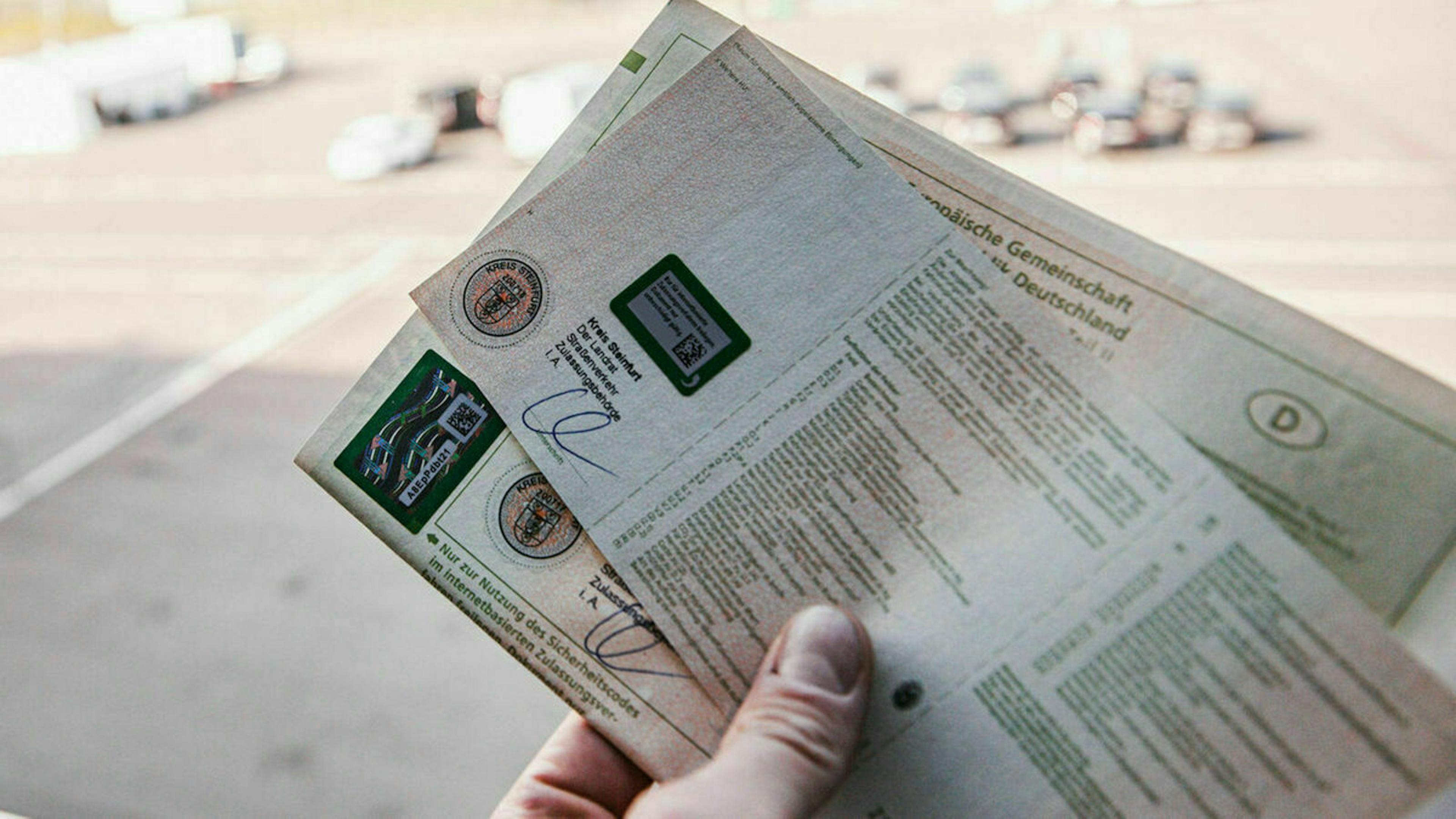 Nahaufnahme einer Hand, die einen Fahrzeugbrief und einen Fahrzeugschein hält