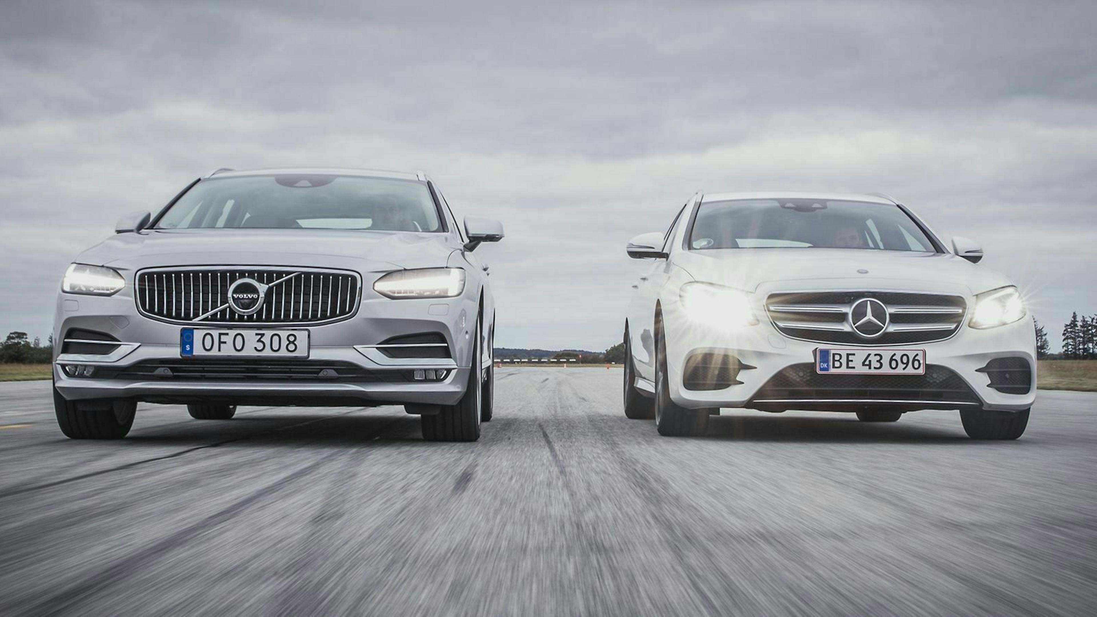 Ein Volvo V90 und eine Mercedes E-Klasse fahren mit eingeschaltetem Abblendlicht eine Straße entlang. 