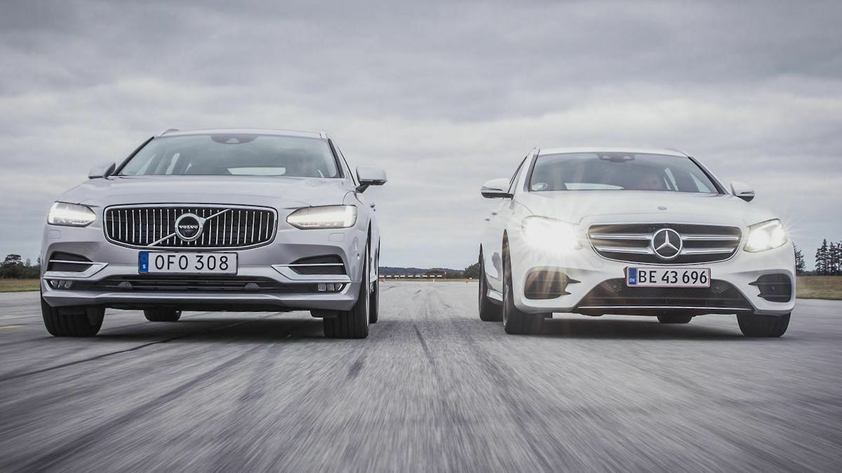 Ein Volvo V90 und eine Mercedes E-Klasse fahren mit eingeschaltetem Abblendlicht eine Straße entlang.