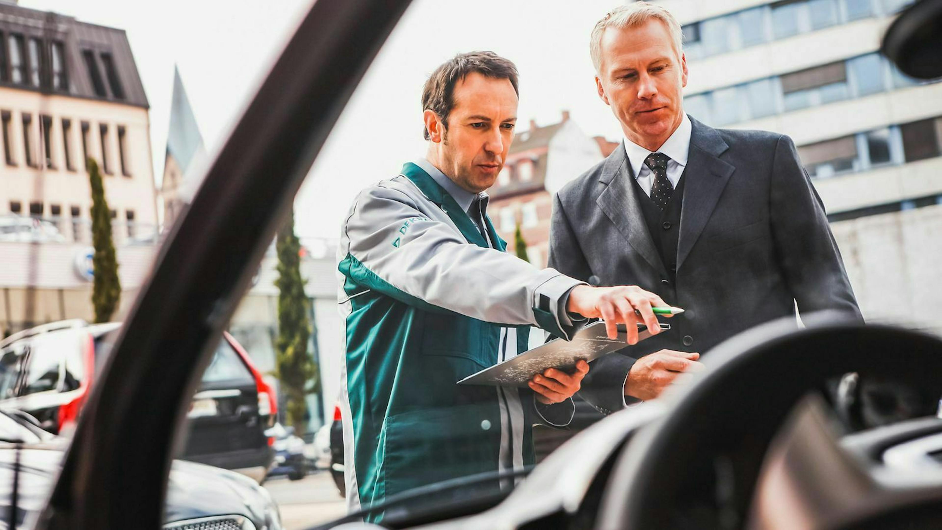 Dekra-Prüfer und Mann im Anzug schauen auf ein Auto.