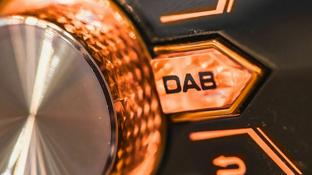 In Nahaufnahme ist ein Lautstärkeregler eines Autoradios zu sehen. Direkt daneben eine Taste mit dem Schriftzug "DAB".
