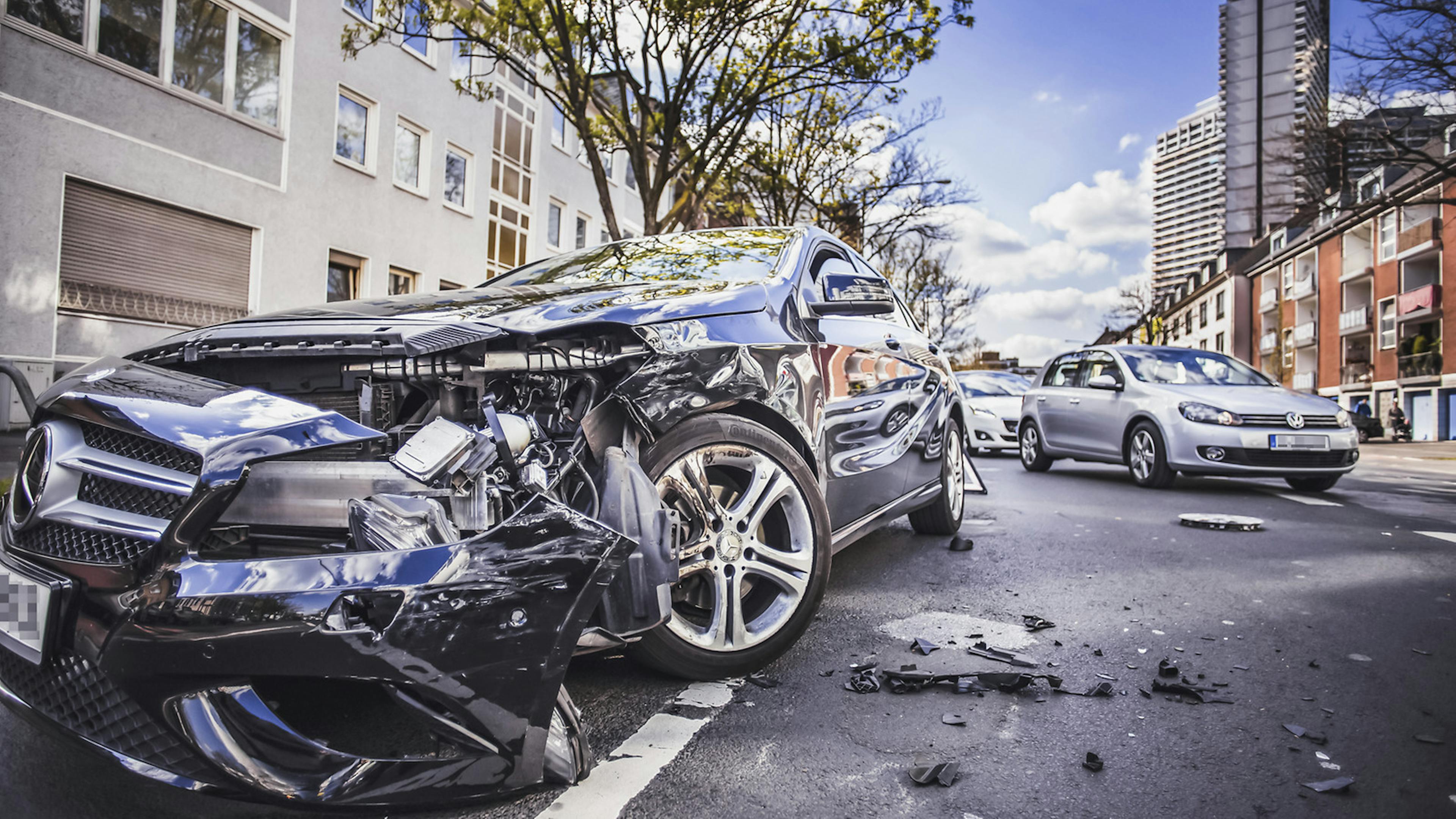 Ein durch einen Unfall zerstörter Mercedes steht am Straßenrand in einer Stadt.