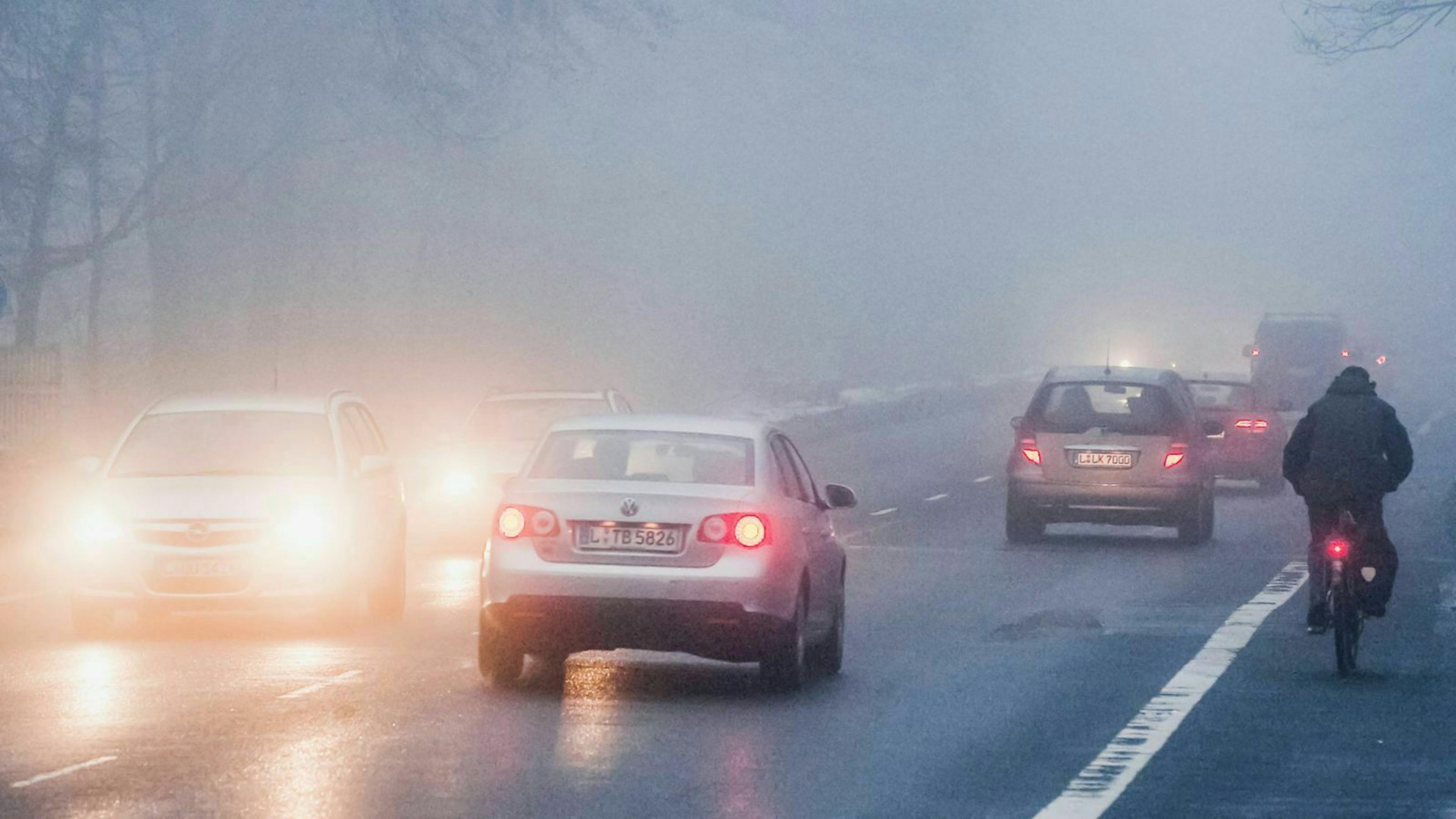 Autos und ein Fahrradfahrer fahren über eine neblige Landstraße.