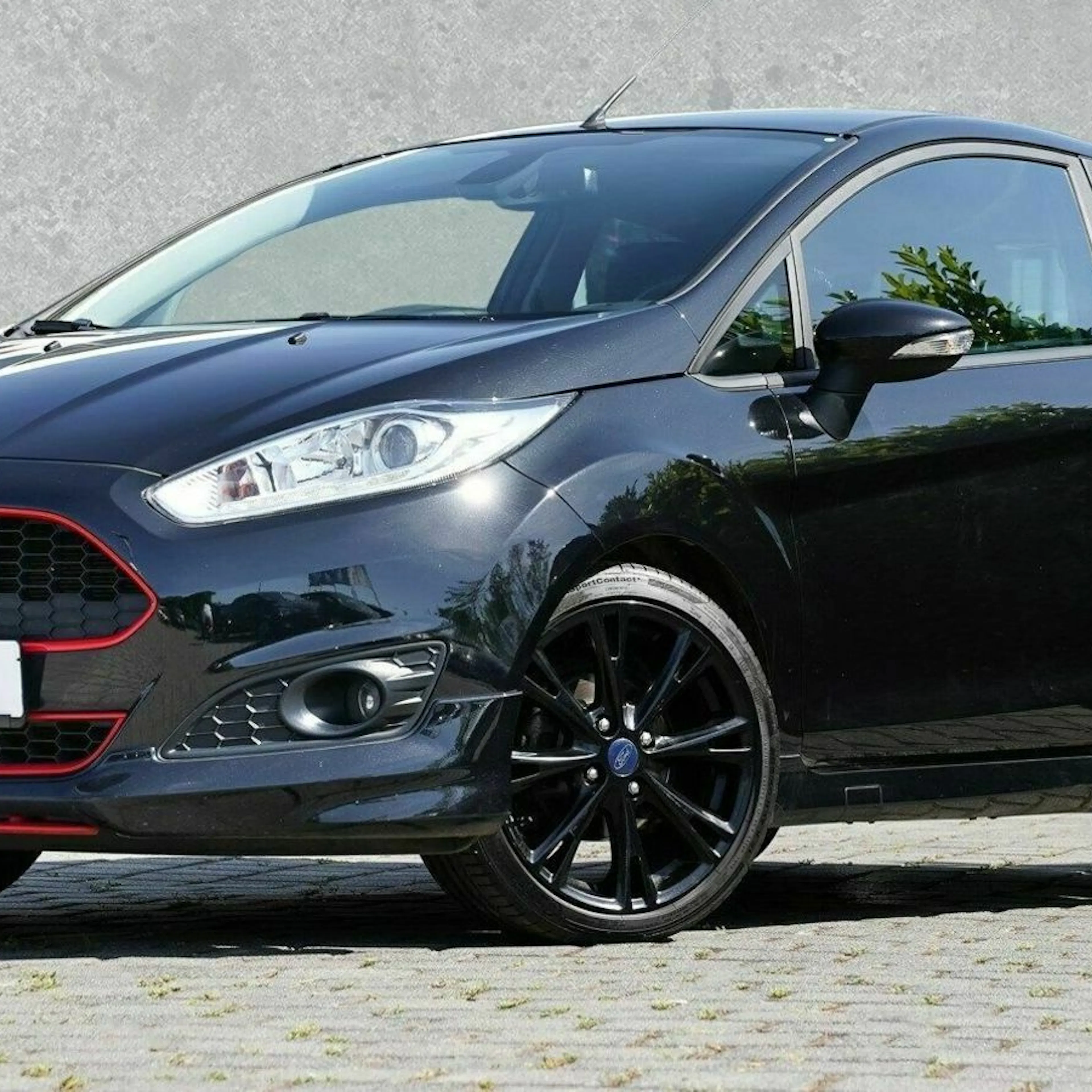 Schwarzer Ford Fiesta mit roten Akzenten, auf einem gepflasterten Platz geparkt, grauer Hintergrund.