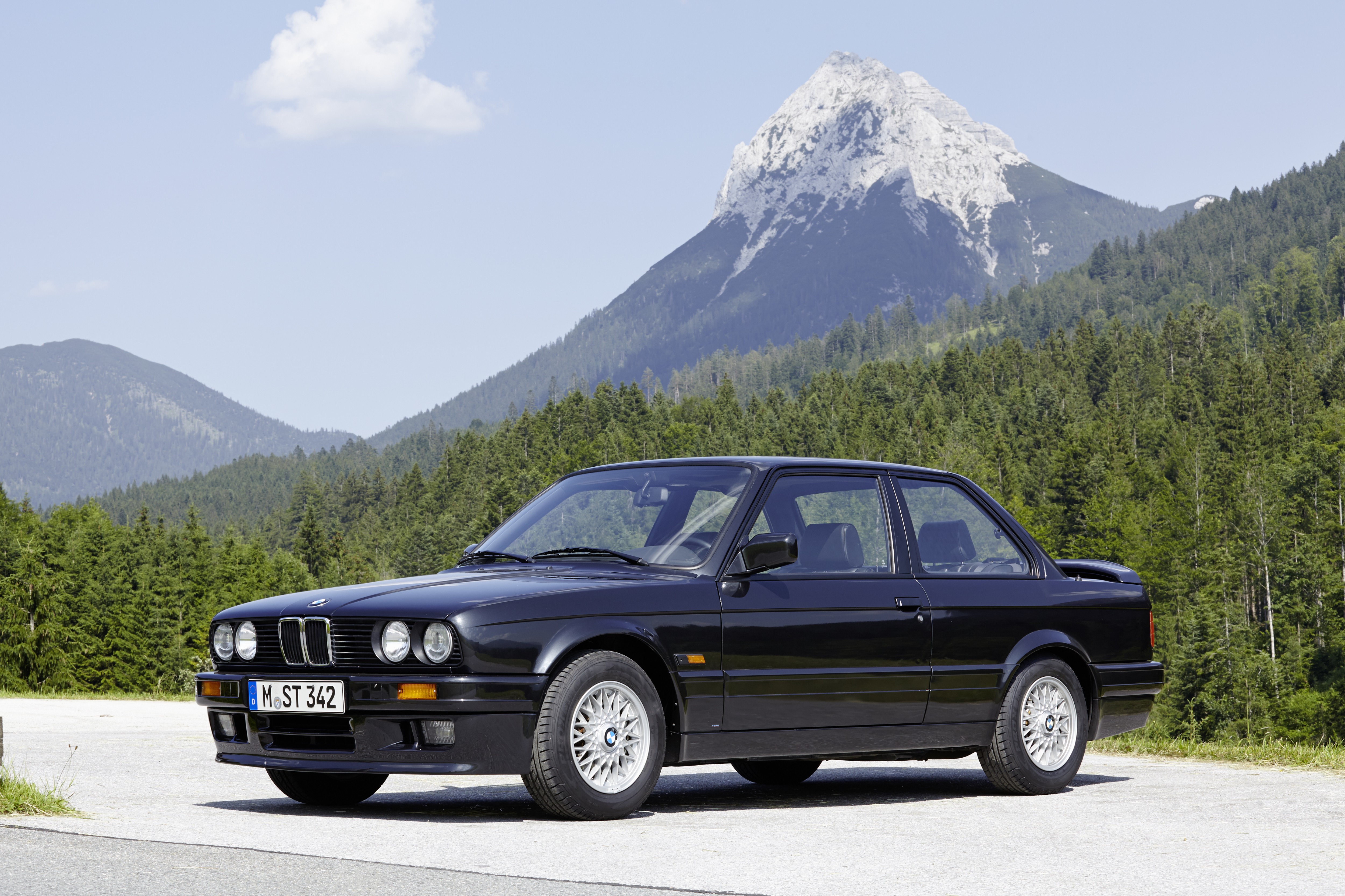 Ein schwarzer BMW 3er E30 steht vor einem Bergpanorama.
