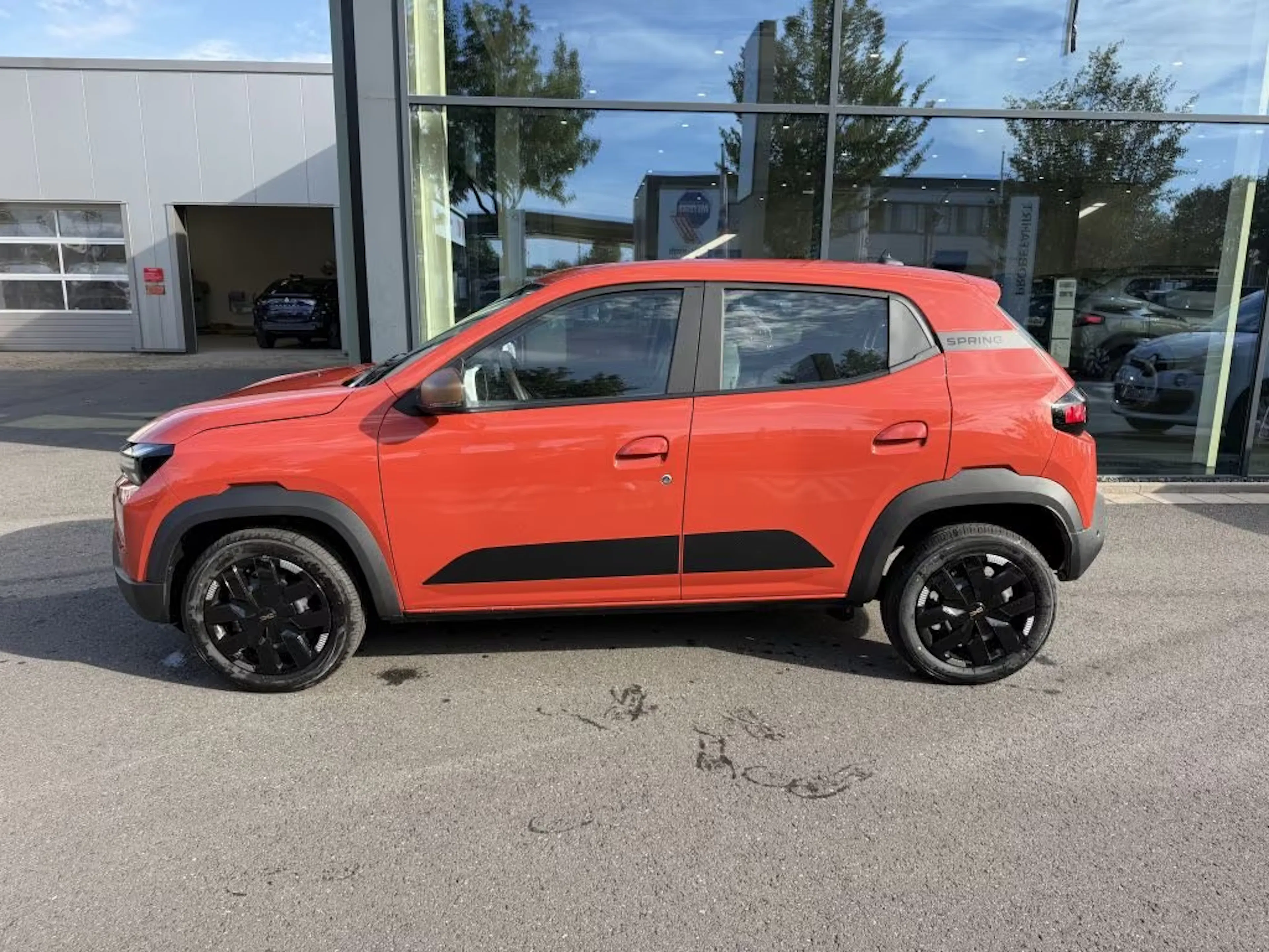 Ein roter Dacia Spring steht vor einem Gebäude mit Glasfassade.