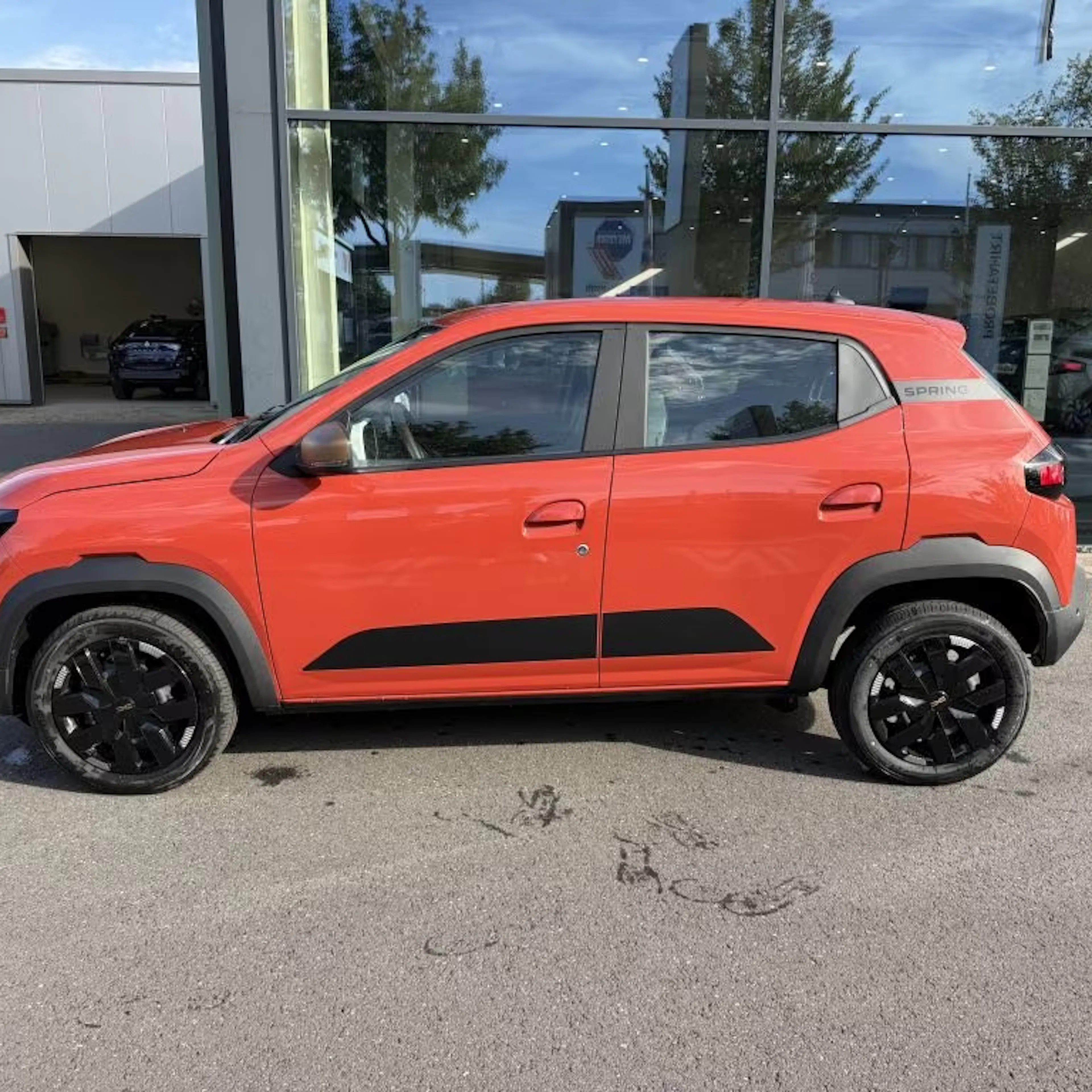 Ein roter Dacia Spring steht vor einem Gebäude mit Glasfassade.