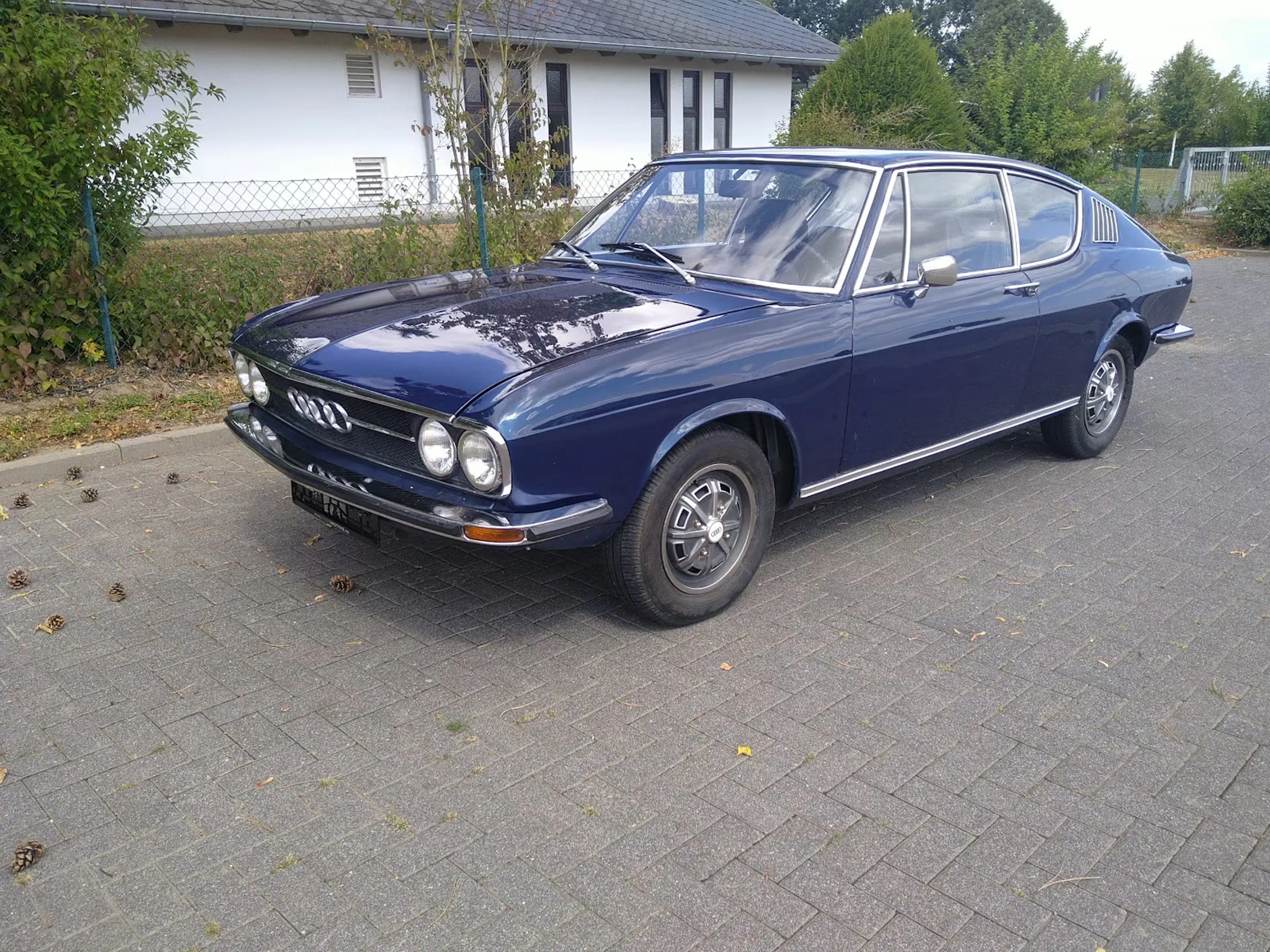 Blauer Audi 100 C1 Coupé steht auf gepflastertem Platz