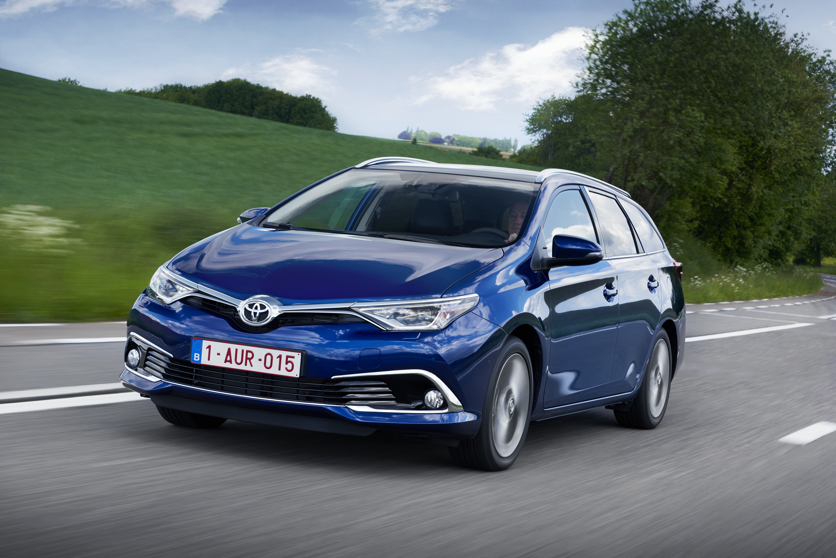 Blauer Toyota Auris Kombi fährt auf einer Landstraße an einer grünen Wiese vorbei.