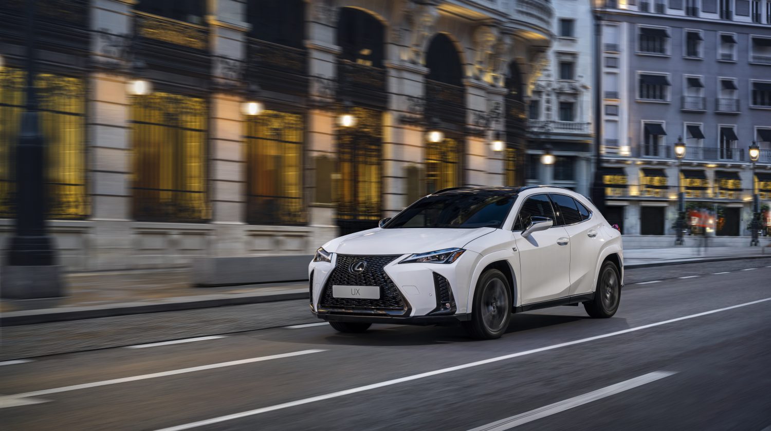 Weißer Lexus UX fährt in der Dämmerung durch eine Stadt.
