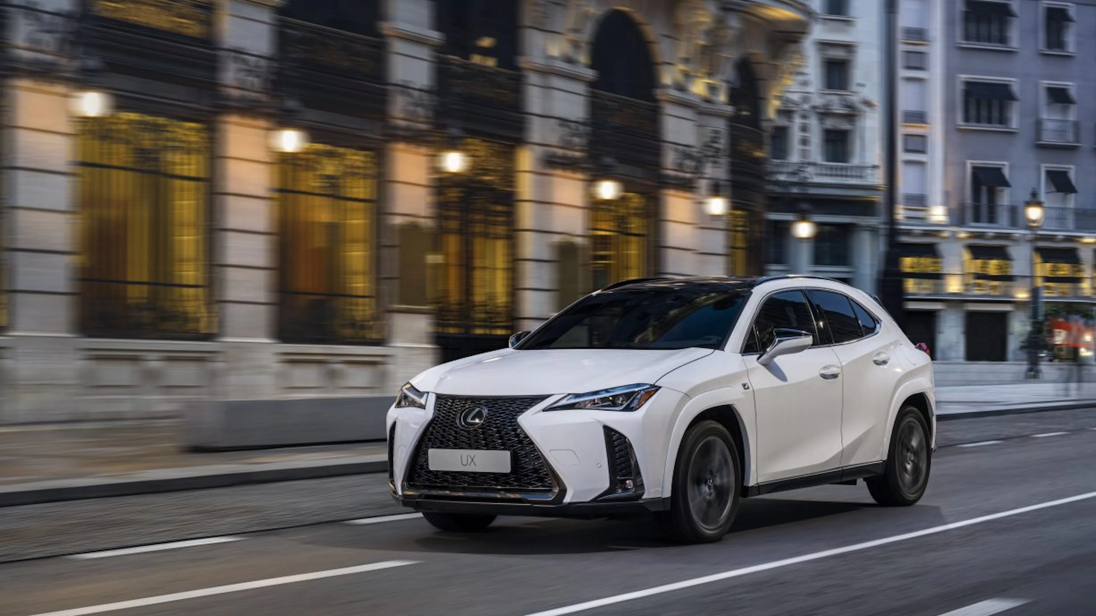 Weißer Lexus UX fährt in der Dämmerung durch eine Stadt.