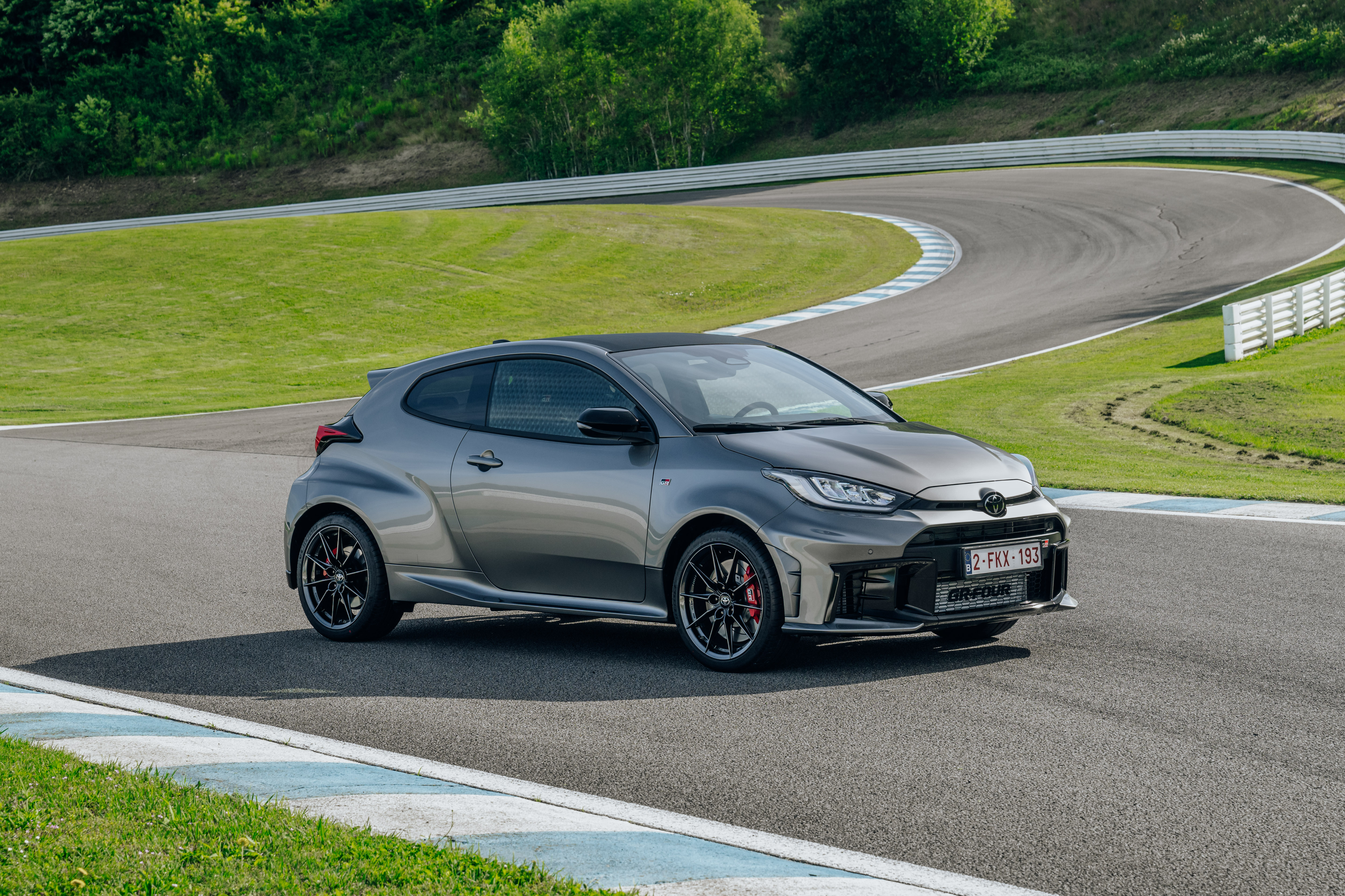Toyota GR Yaris in Grau fährt dynamisch auf einer Rennstrecke, Seitenansicht von vorne