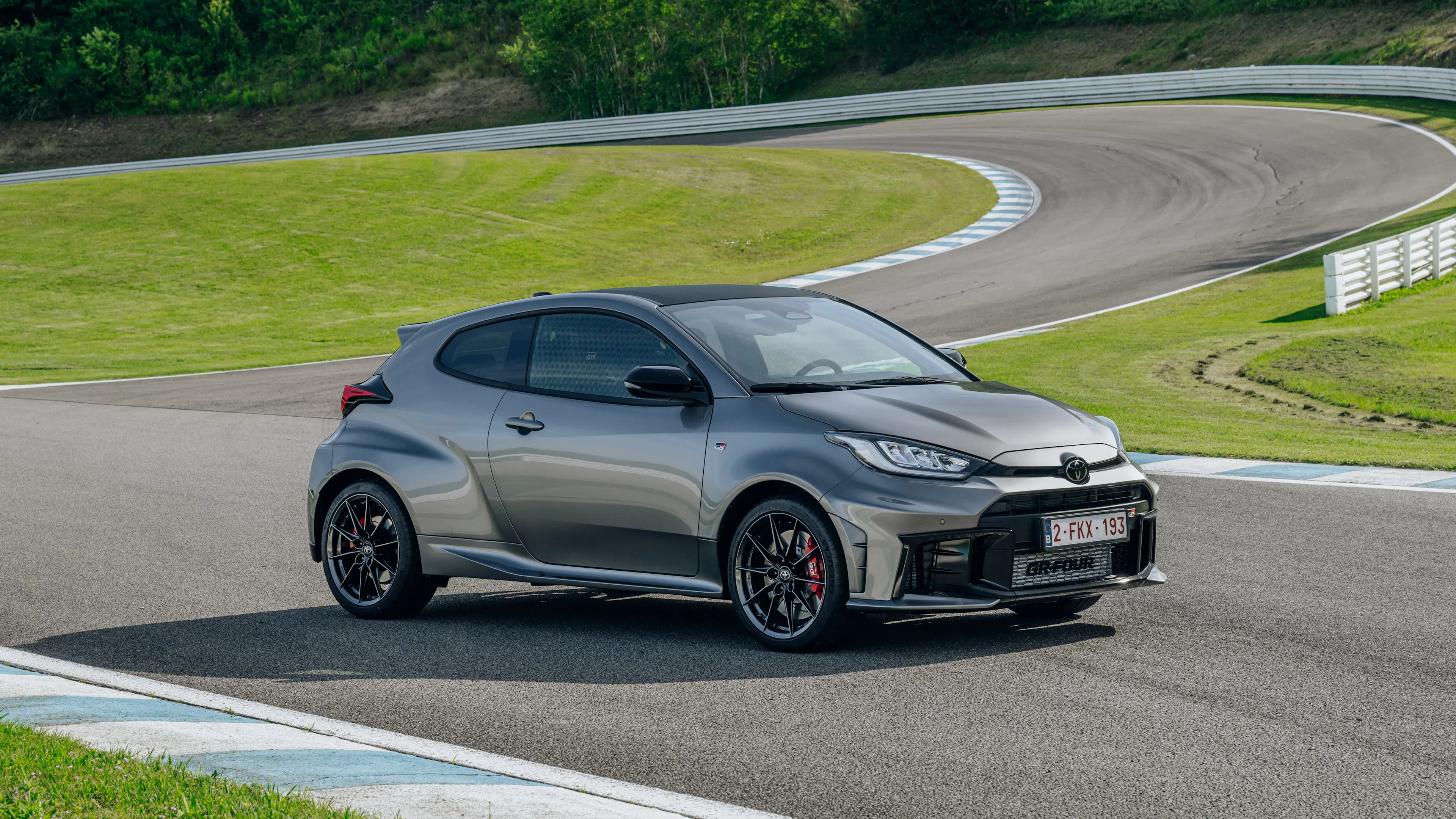 Toyota GR Yaris in Grau fährt dynamisch auf einer Rennstrecke, Seitenansicht von vorne