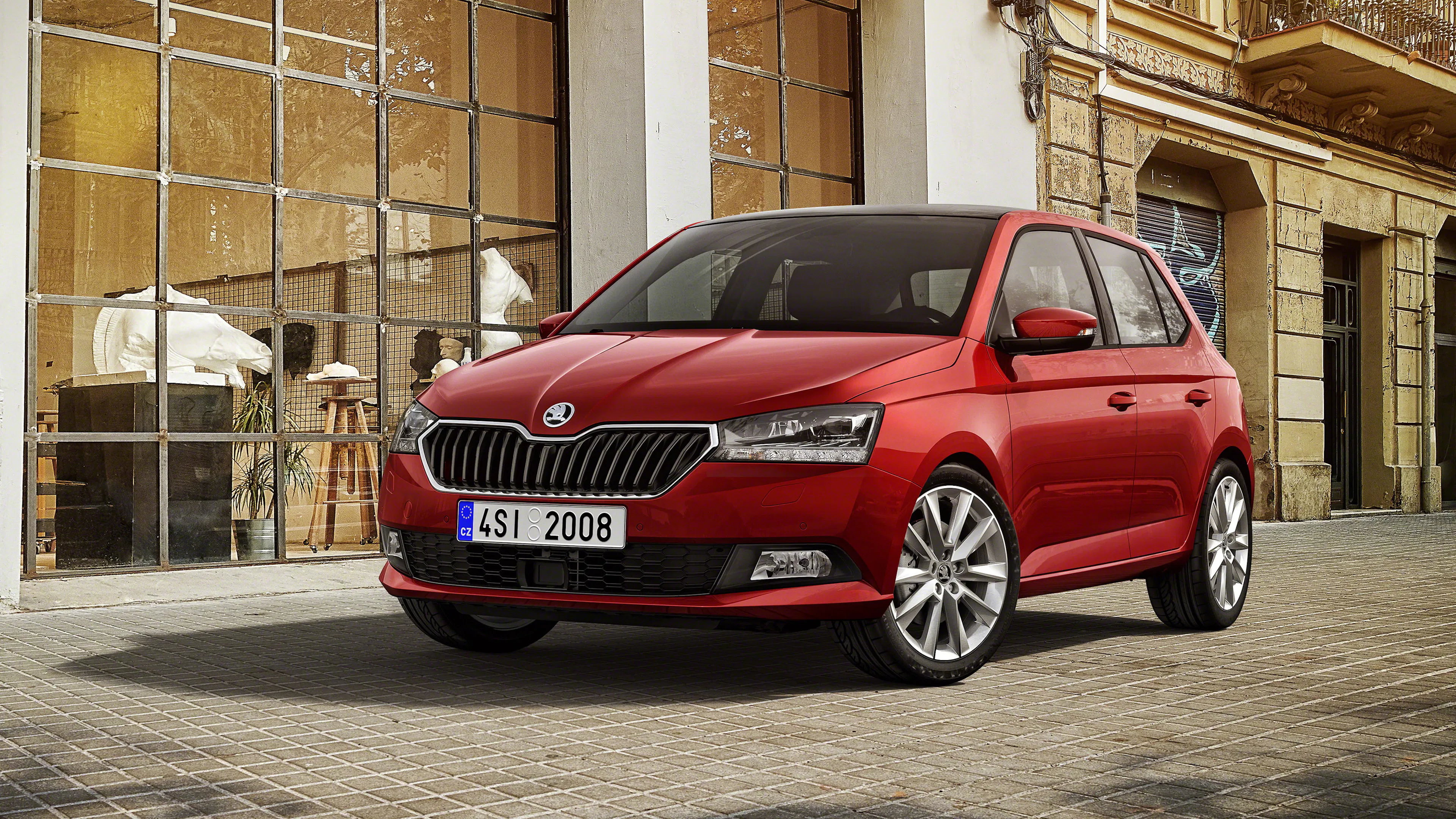 Roter Škoda Fabia III steht auf Kopfsteinpflaster vor einem Altbau mit großer Sprossenfassade.