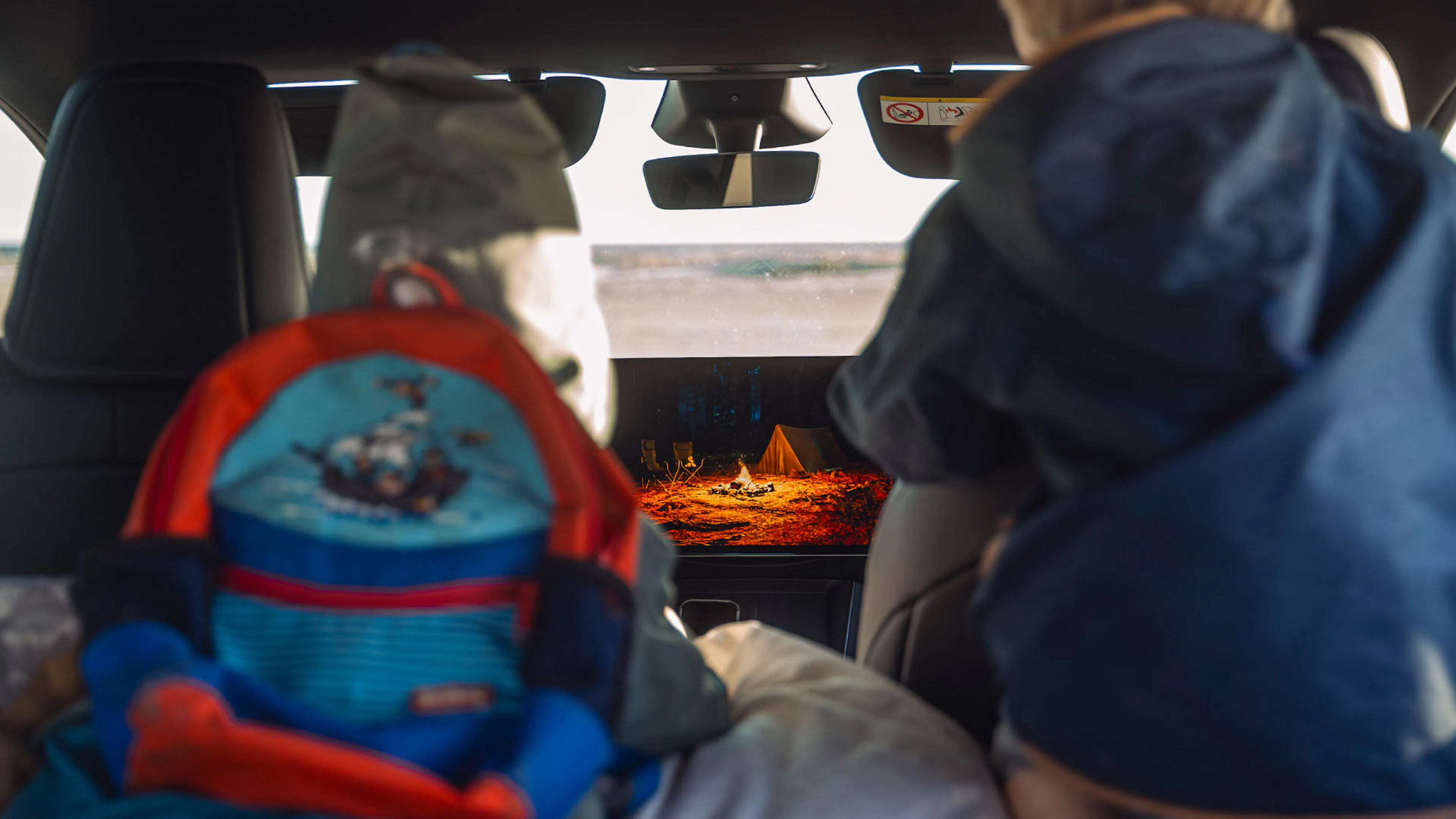 Zwei Kinder schauen auf den Bildschirm des Tesla Model Y, das eine Lagerfeuerszene am Zelt zeigt.