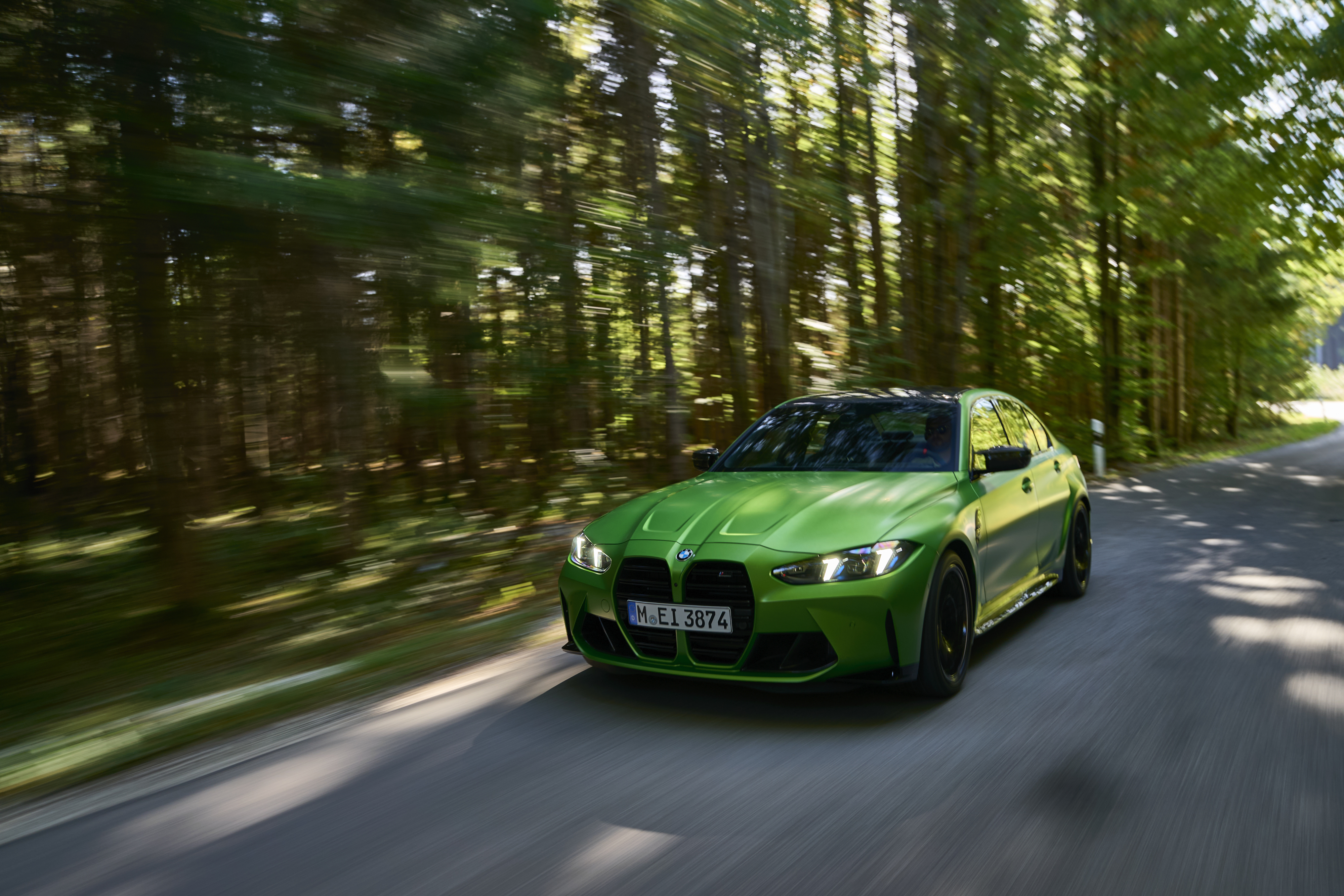 BMW-M3-Limousine fährt dynamisch auf einer Waldstraße, Frontansicht