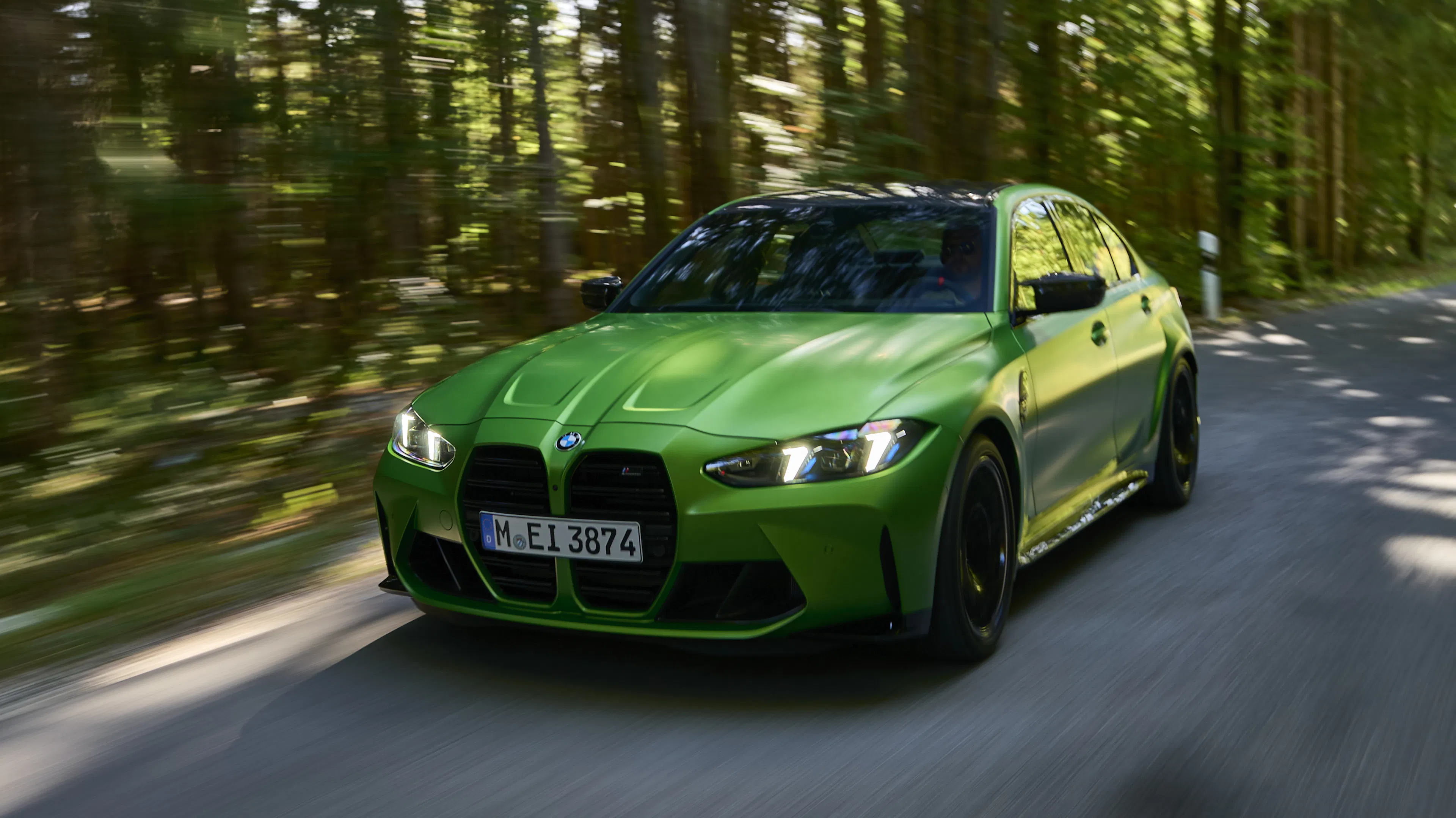 BMW-M3-Limousine fährt dynamisch auf einer Waldstraße, Frontansicht