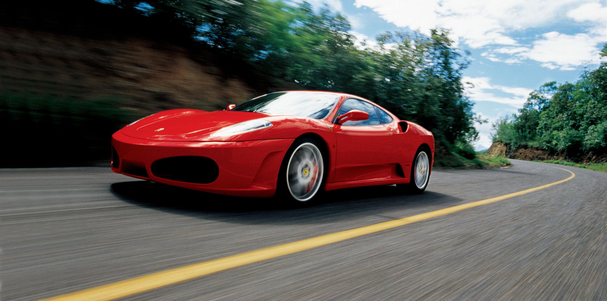 Ein roter Ferrari F430 fährt auf einer Landstraße.