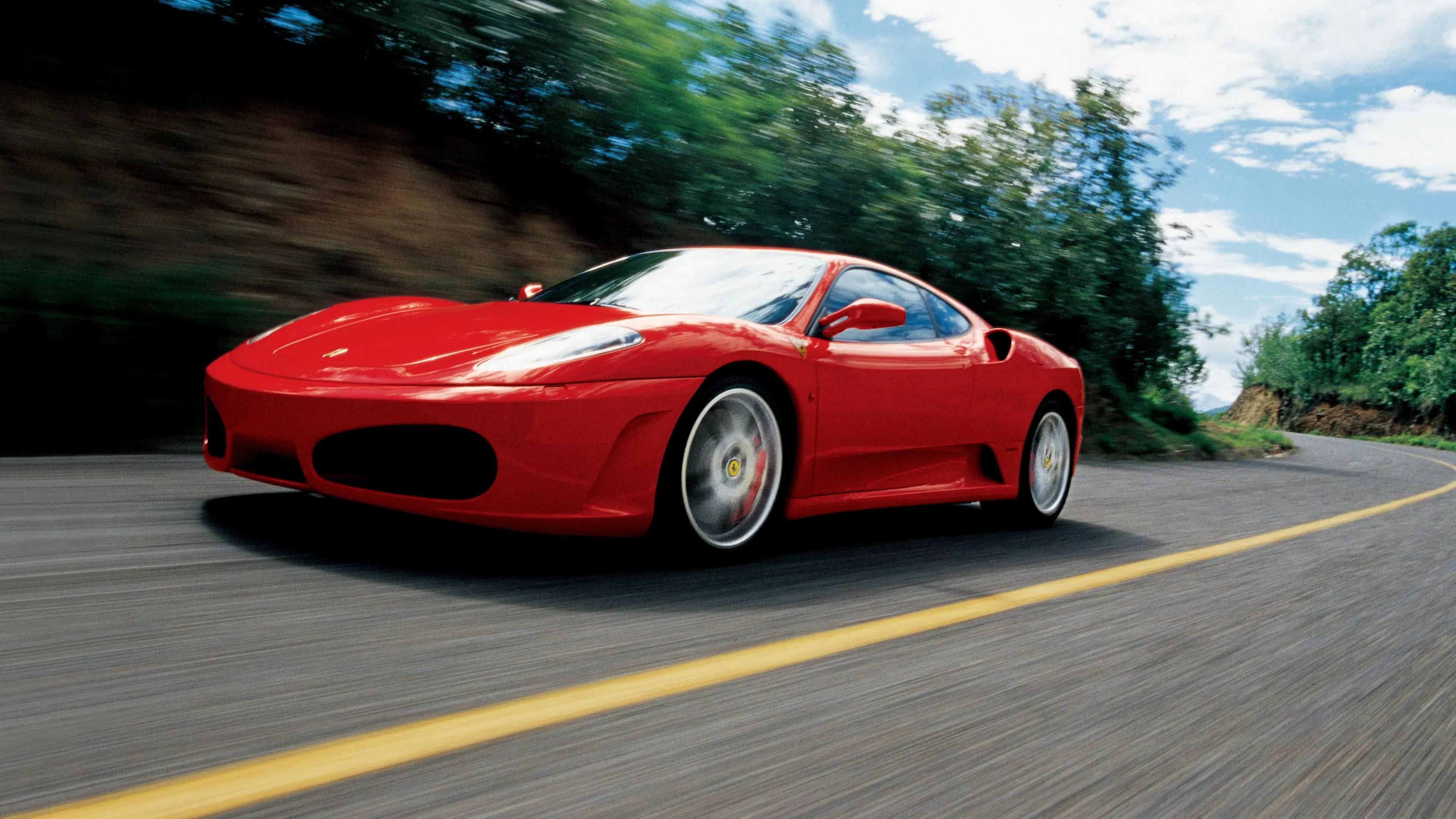 Ein roter Ferrari F430 fährt auf einer Landstraße.