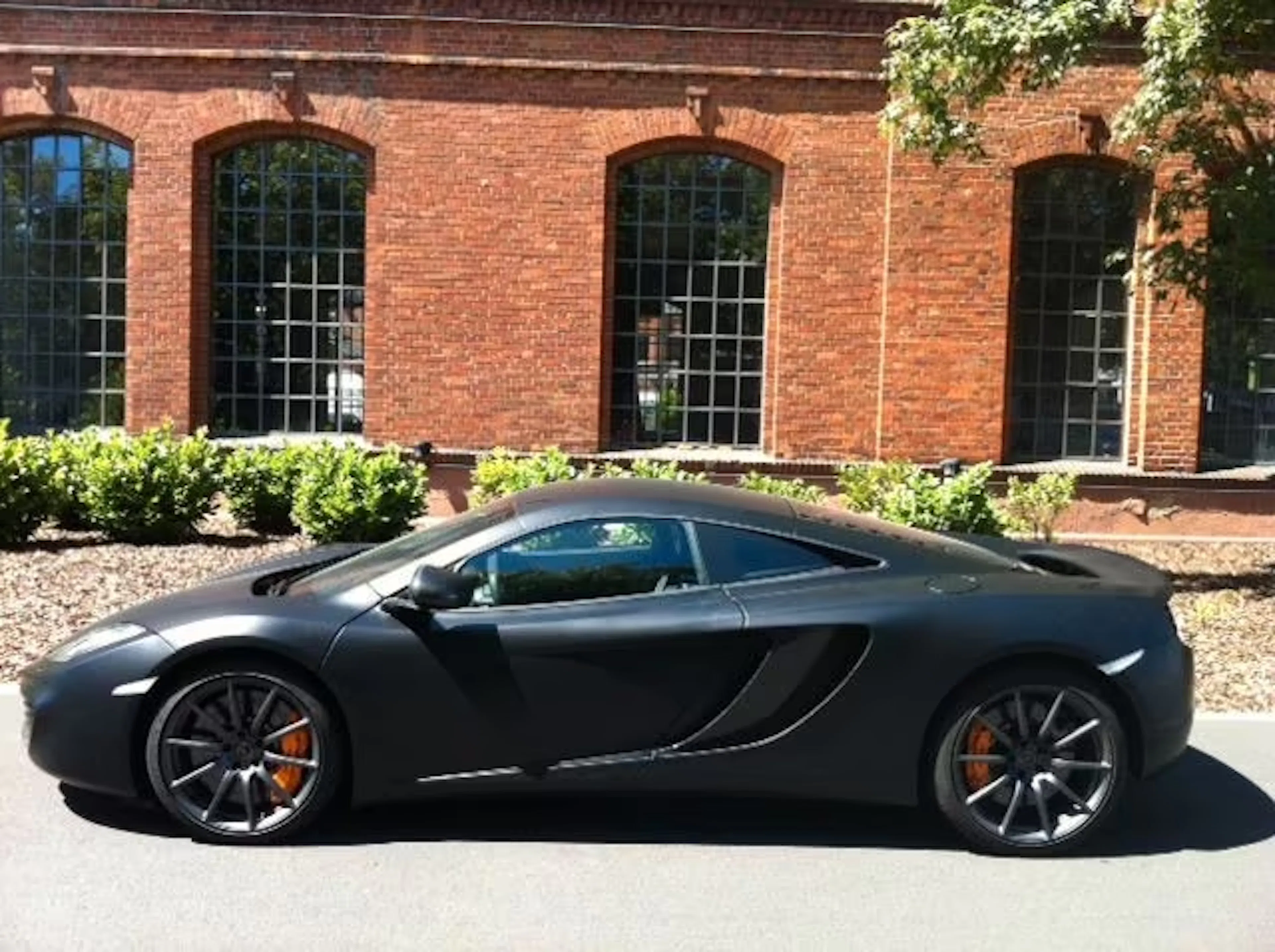 Ein schwarzer McLaren MP4 12C steht vor einem roten Backsteingebäude.