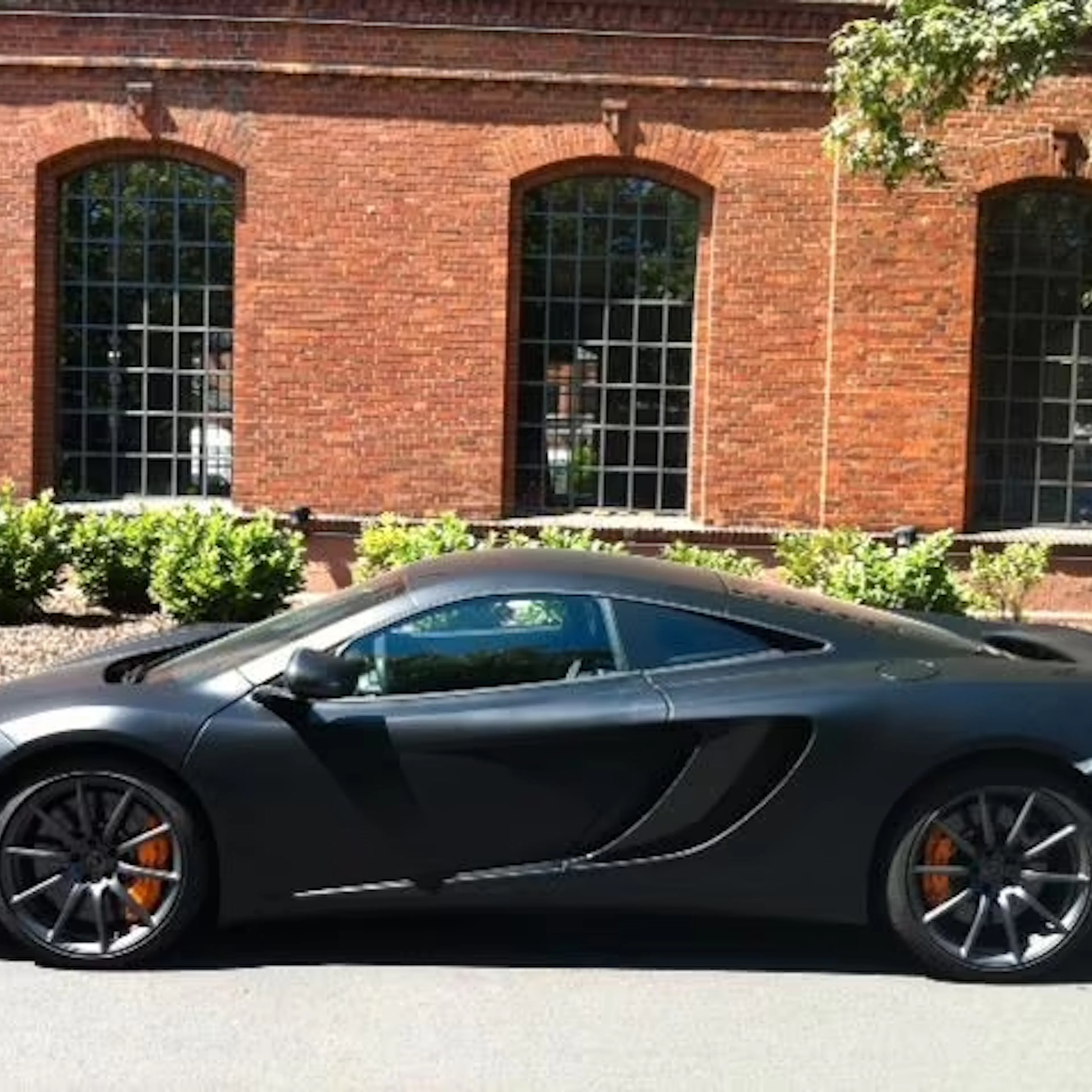Ein schwarzer McLaren MP4 12C steht vor einem roten Backsteingebäude.