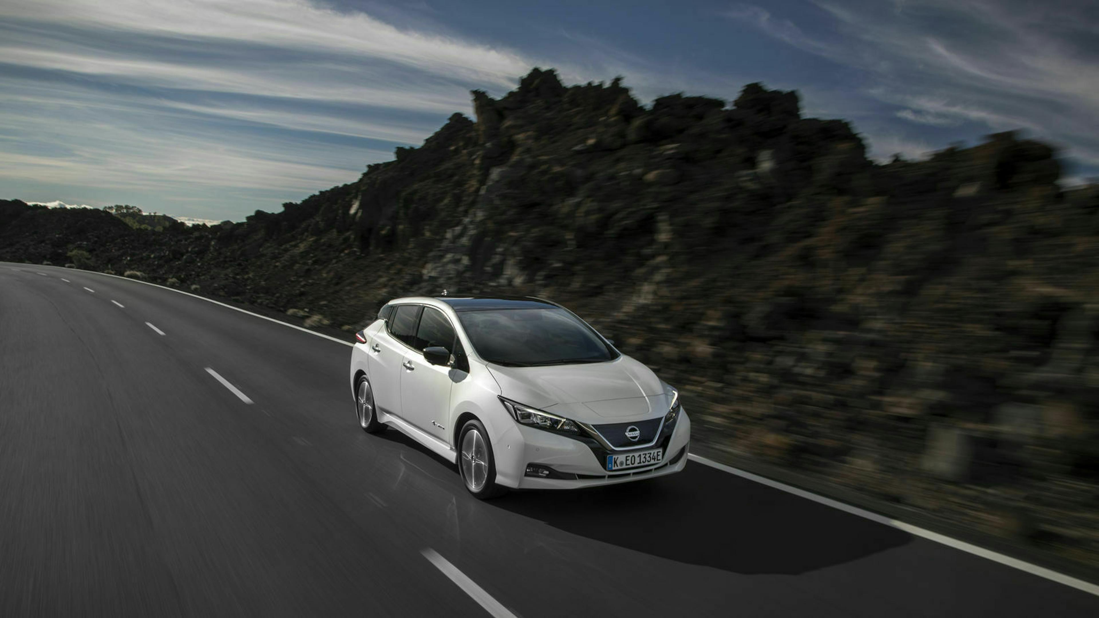 Ein weißer Nissan Leaf fährt eine Landstraße entlang durch eine Landschaft mit Klippen