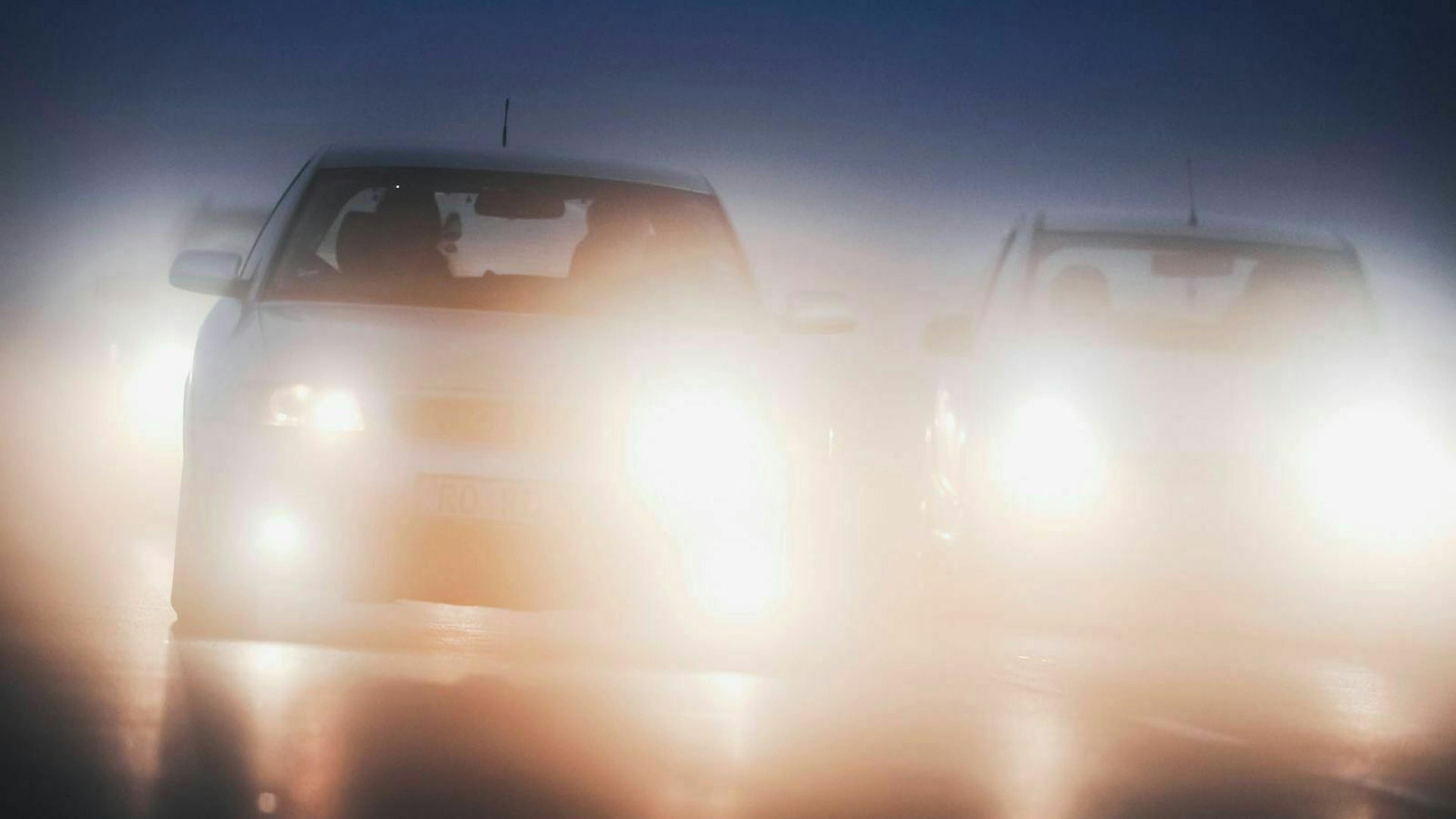 Mit blendenden Scheinwerfern fahren zwei Autos nebeneinander auf einer dunklen Straße.