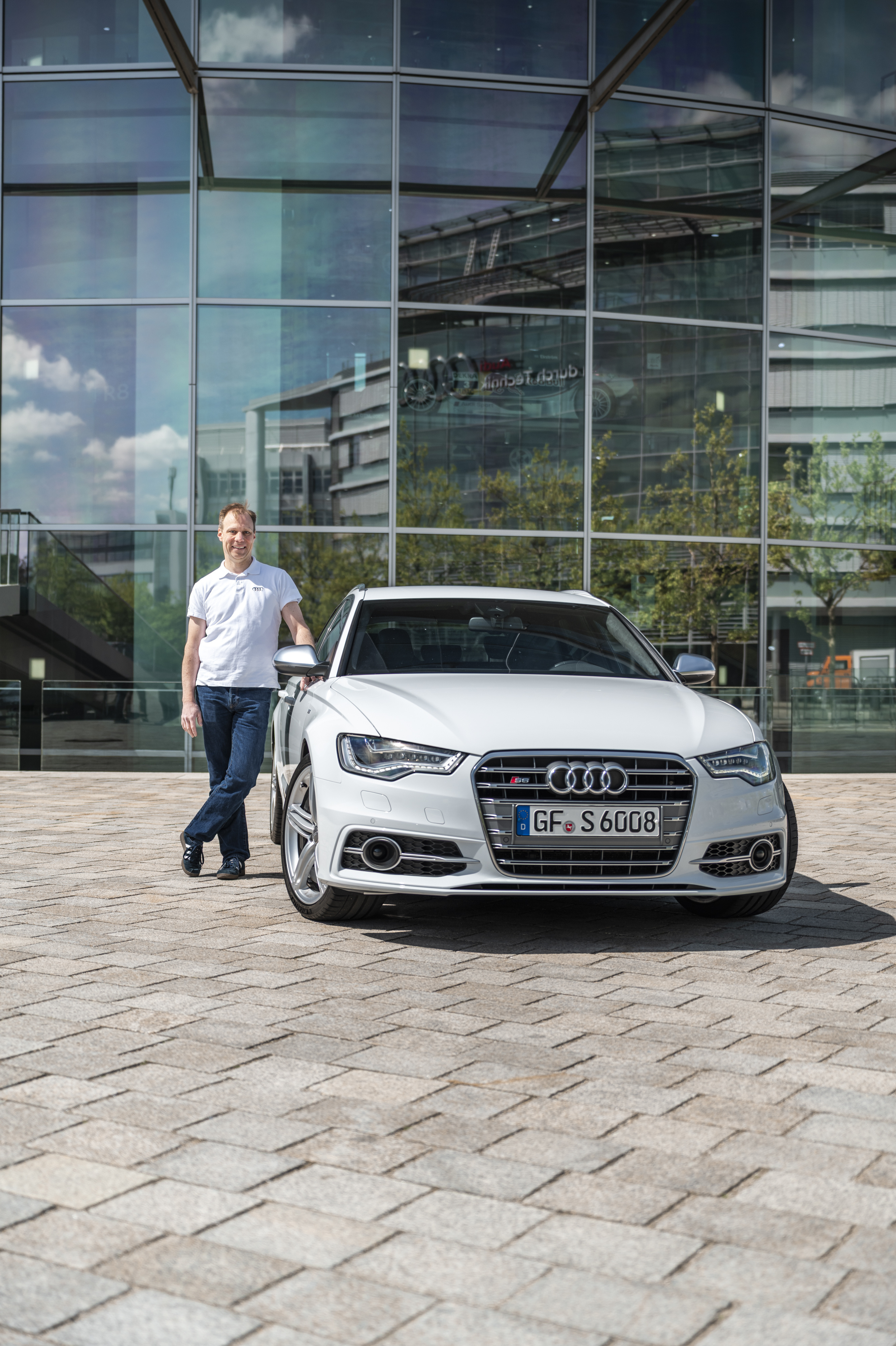 Weißer Audi S6 C7 mit Besitzer, frontal fotografiert vor einer gebogenen Glasfassade.