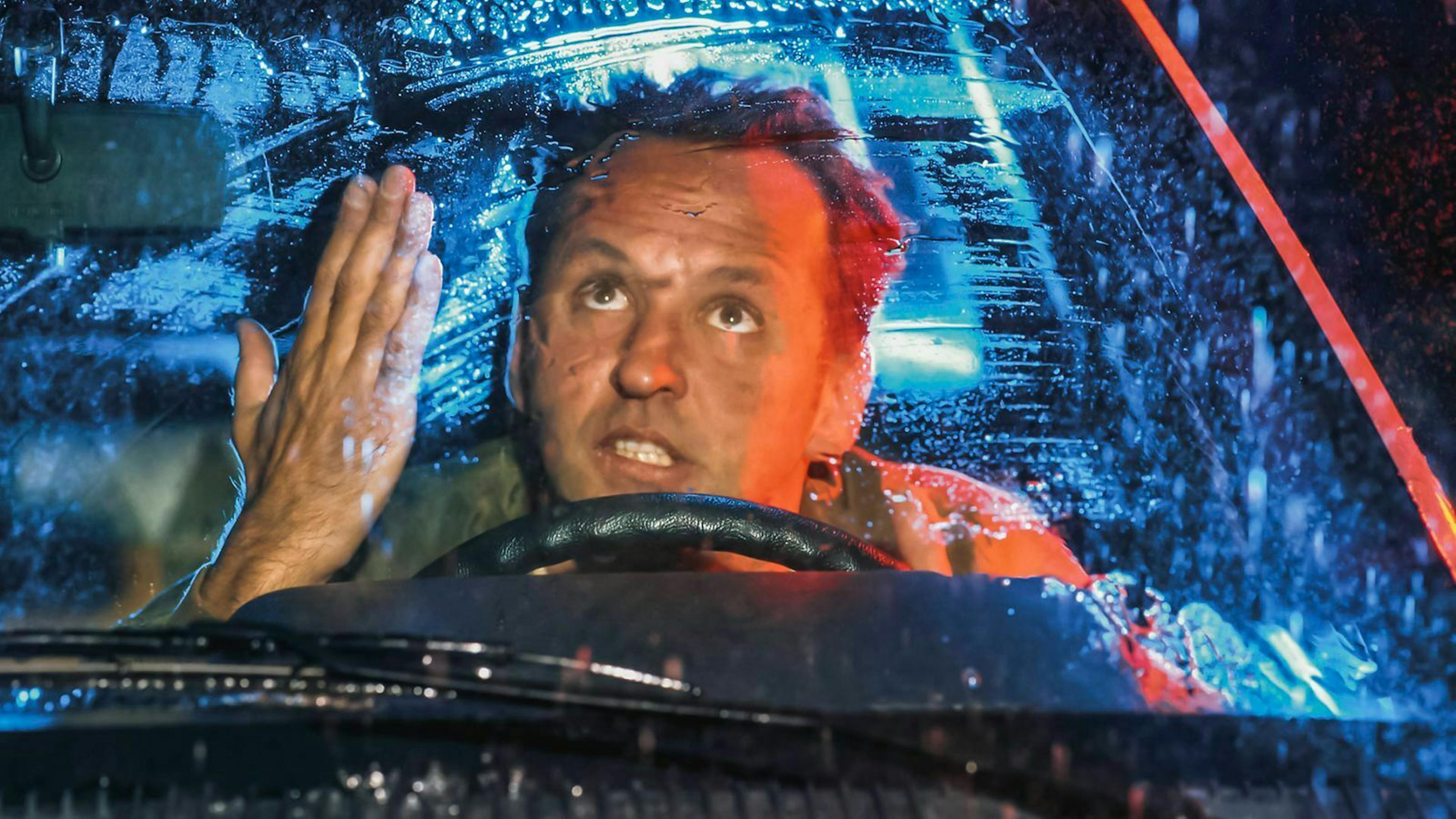 Ein Mann ärgert sich in seinem Auto über die schlechte Sicht bei Regen.