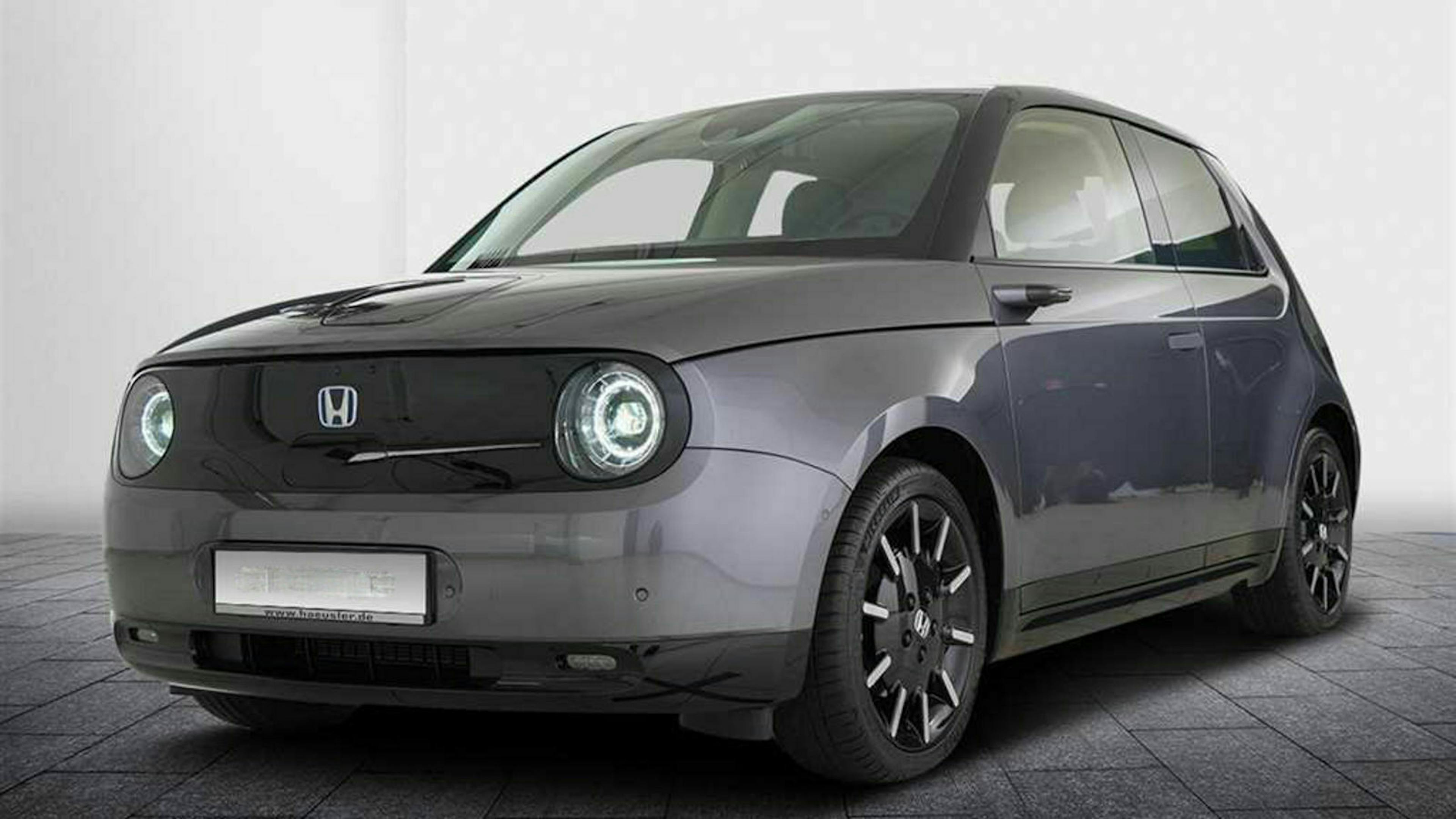 Ein dunkelgrauer Honda E steht vor einer weißen Wand.